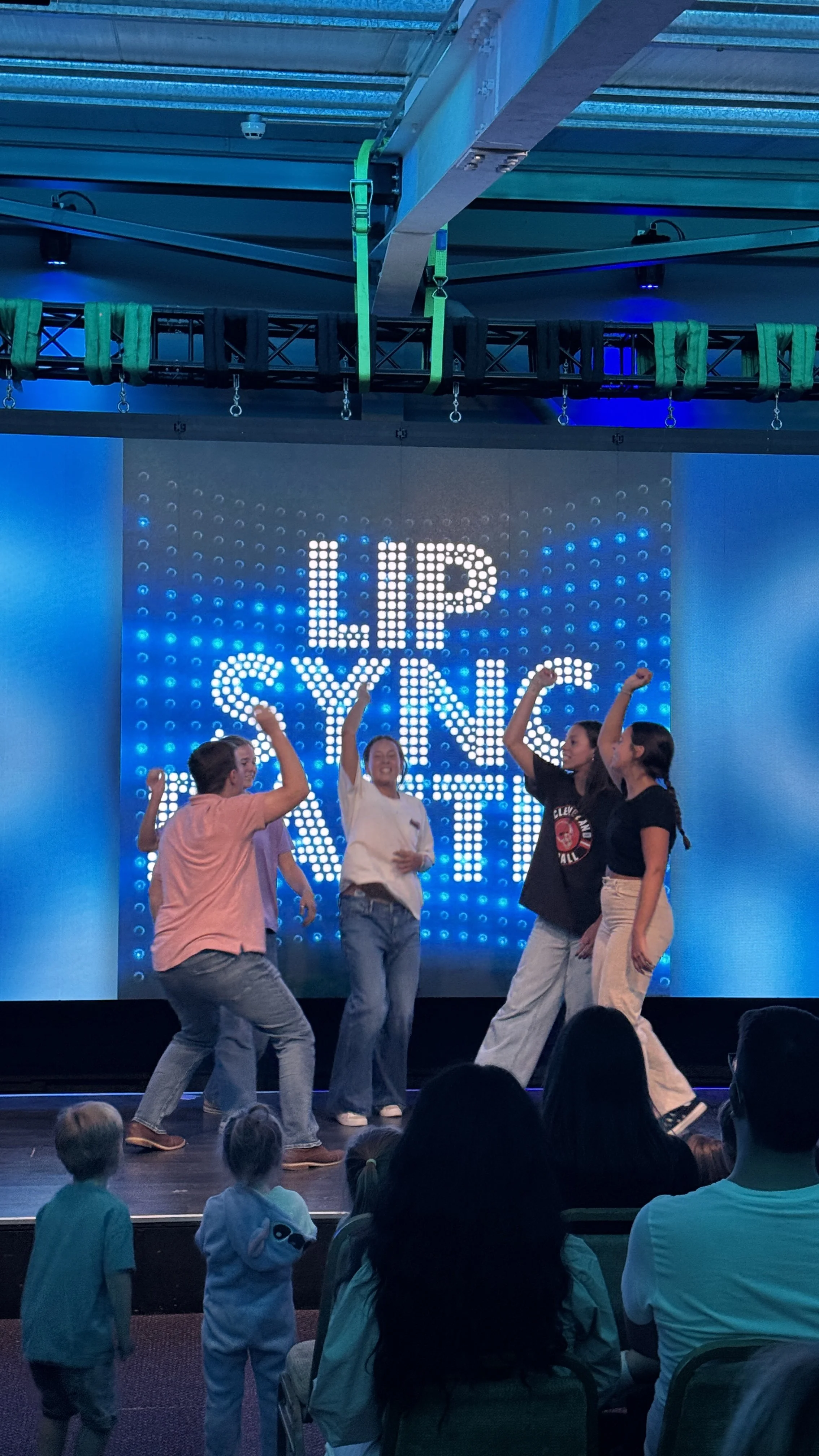 Group of people dancing on stage during the lip sync battle, with audience in front and a digital screen in the background displaying 'LIP SYNC BATTLE'.