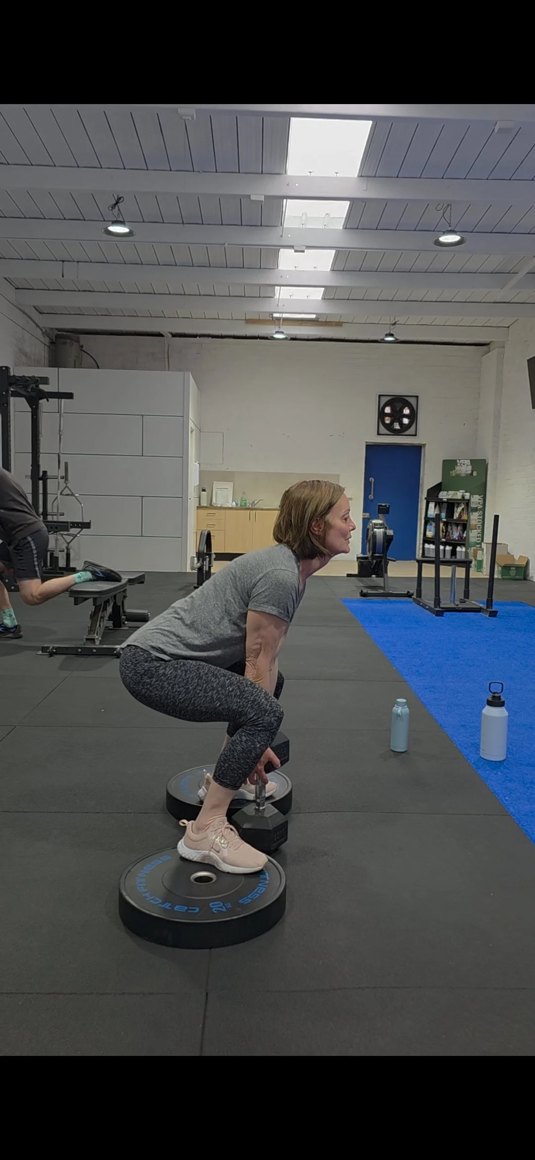 Woman performing a squat exercise with weights in a gym environment.