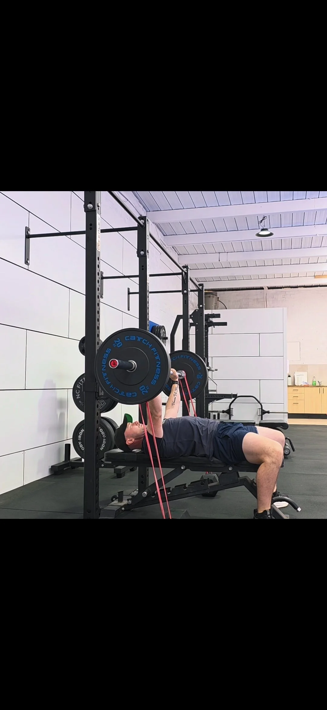 A man lifting weights using resistance bands in a gym, lying on a weight bench with a power rack behind him.