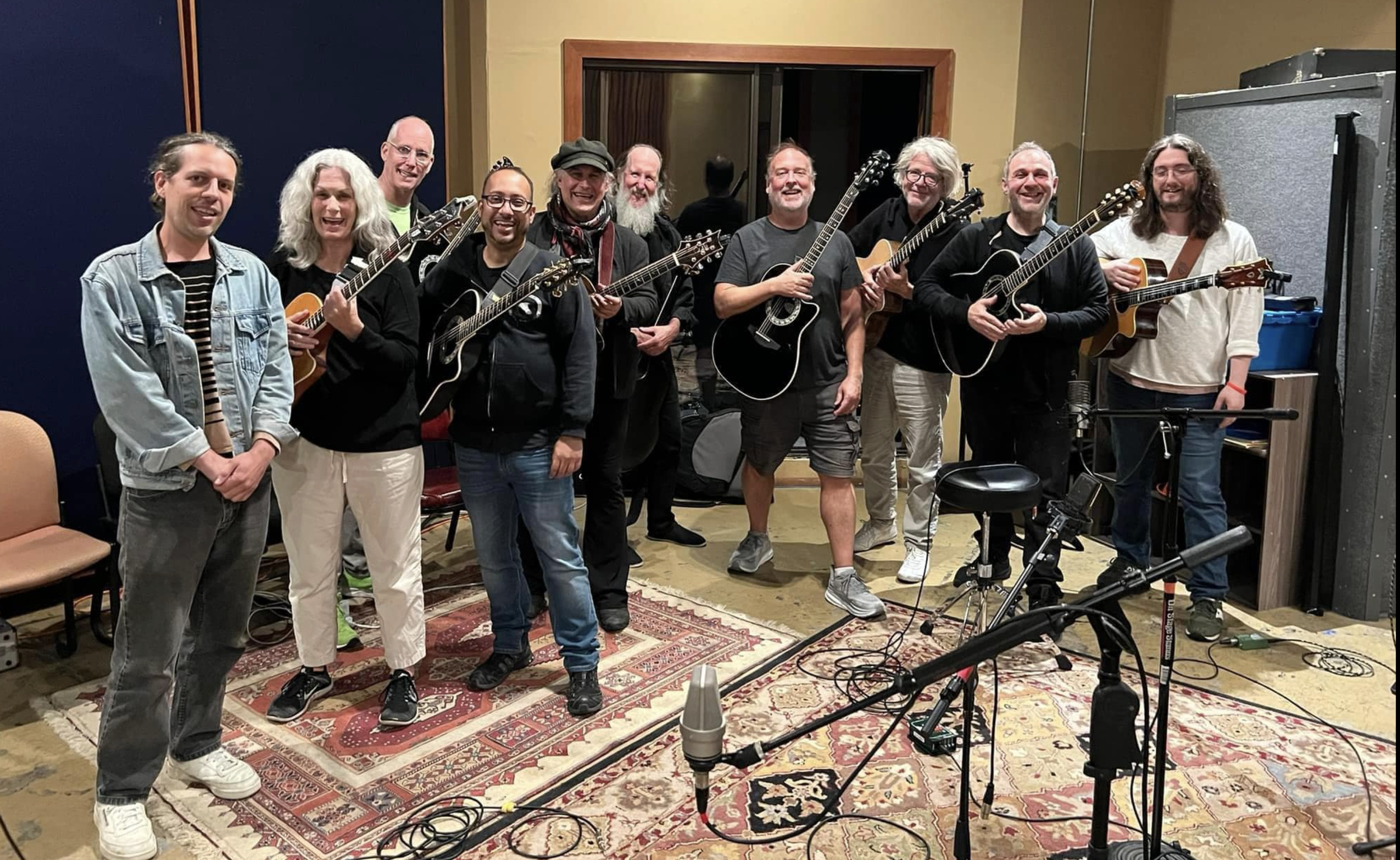 Group of ten musicians with guitars and ukulele in recording studio, smiling after playing or rehearsal