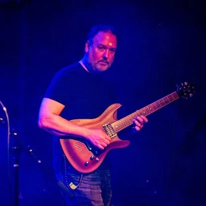 Man playing an electric guitar on stage with blue lighting.