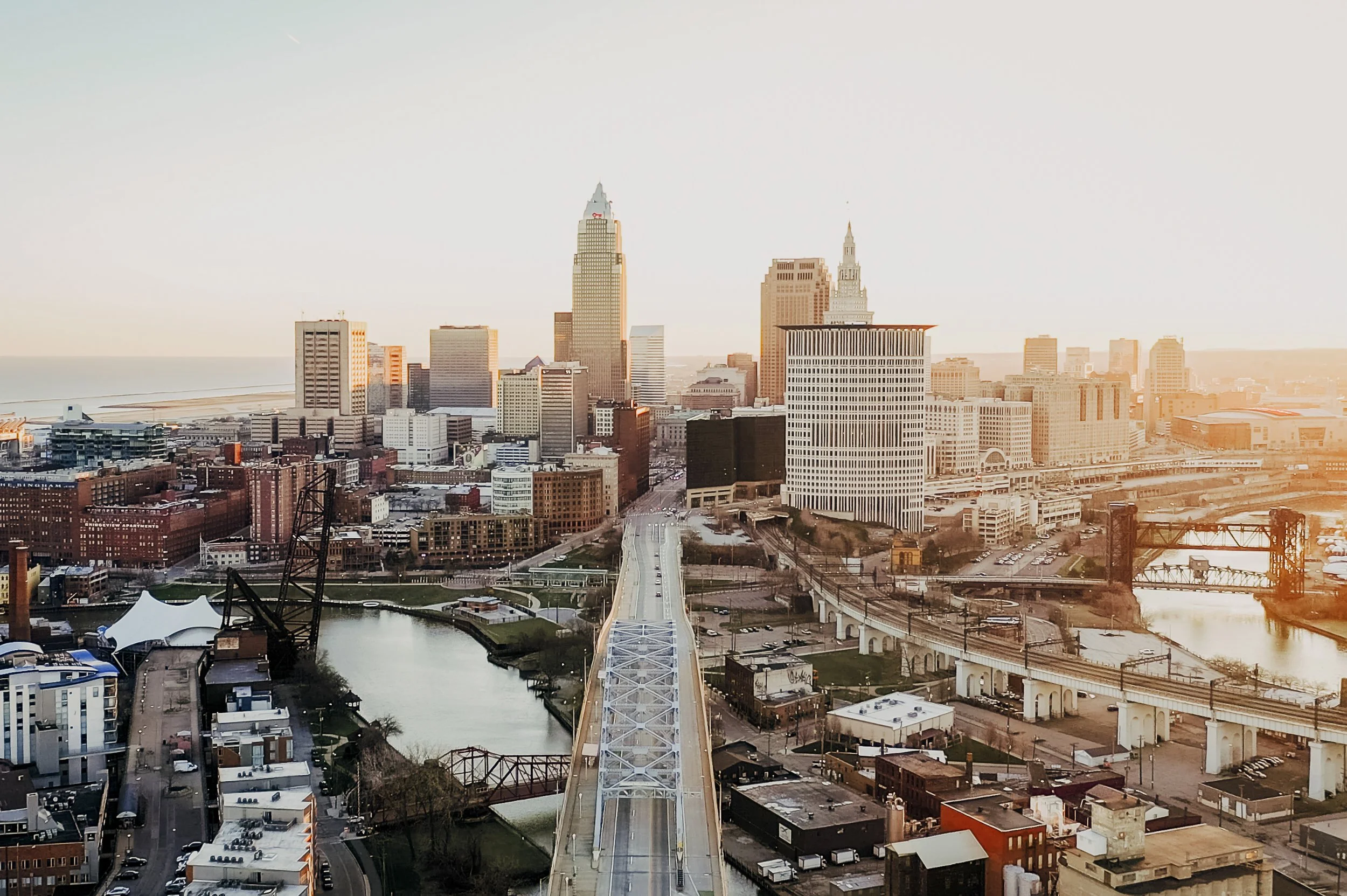 Sunset view of downtown Cleveland, Ohio, with skyscrapers, bridges, and rivers in the foreground.