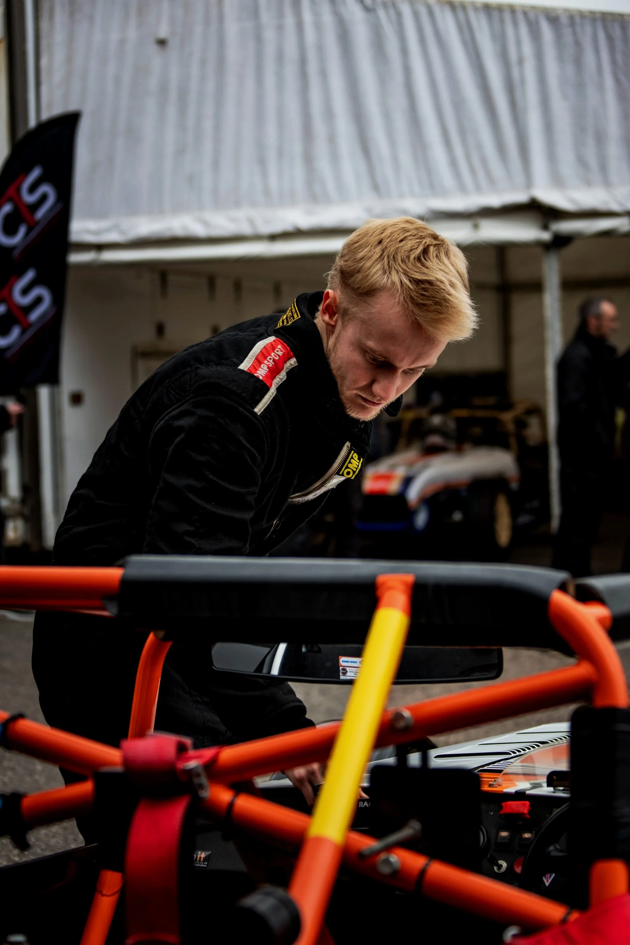 Thomas Horton in a black racing suit stepping into his Caterham at a race track.