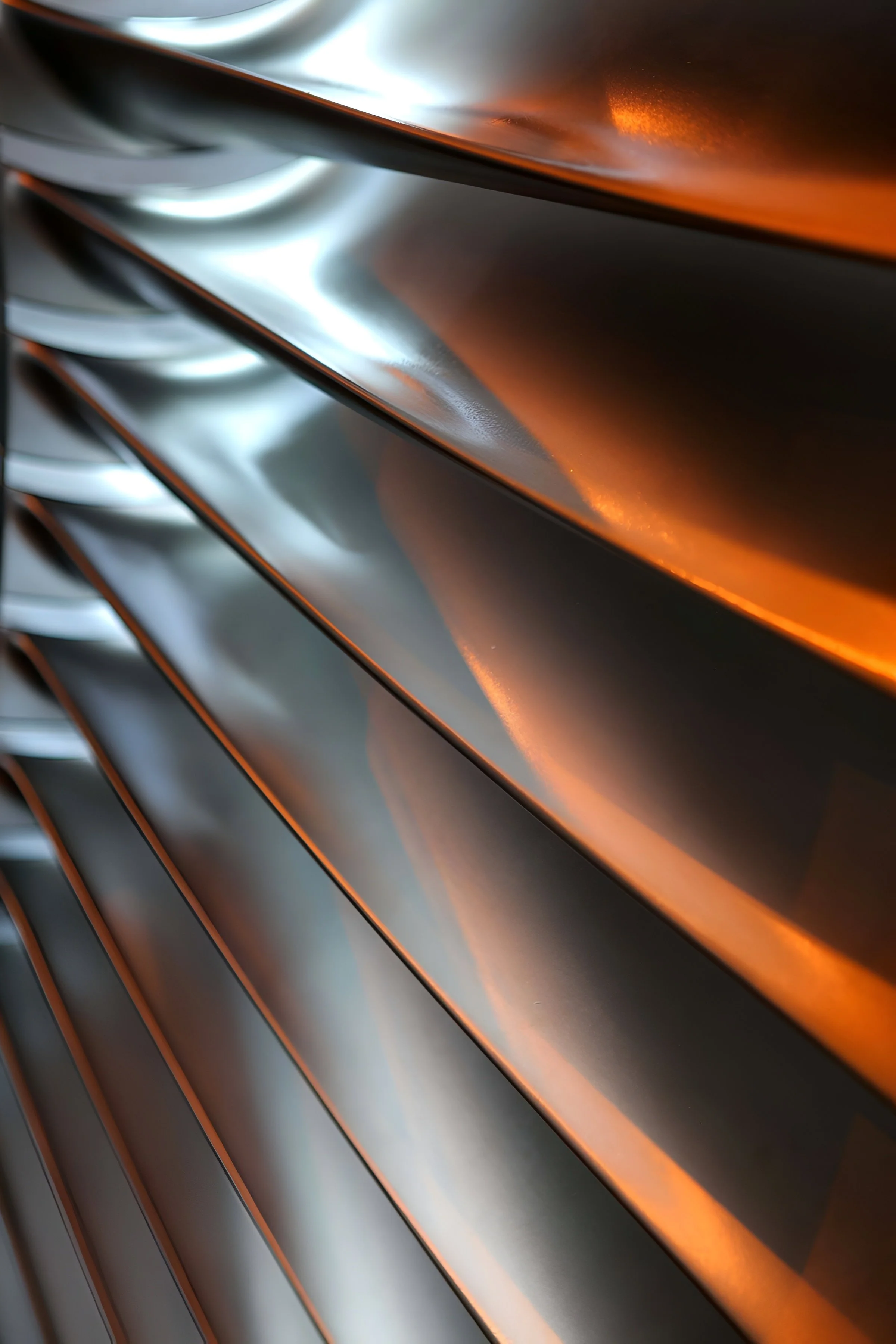 Close-up of metallic fins or slats, reflecting light with a shiny, smooth surface, featuring orange and silver tones.