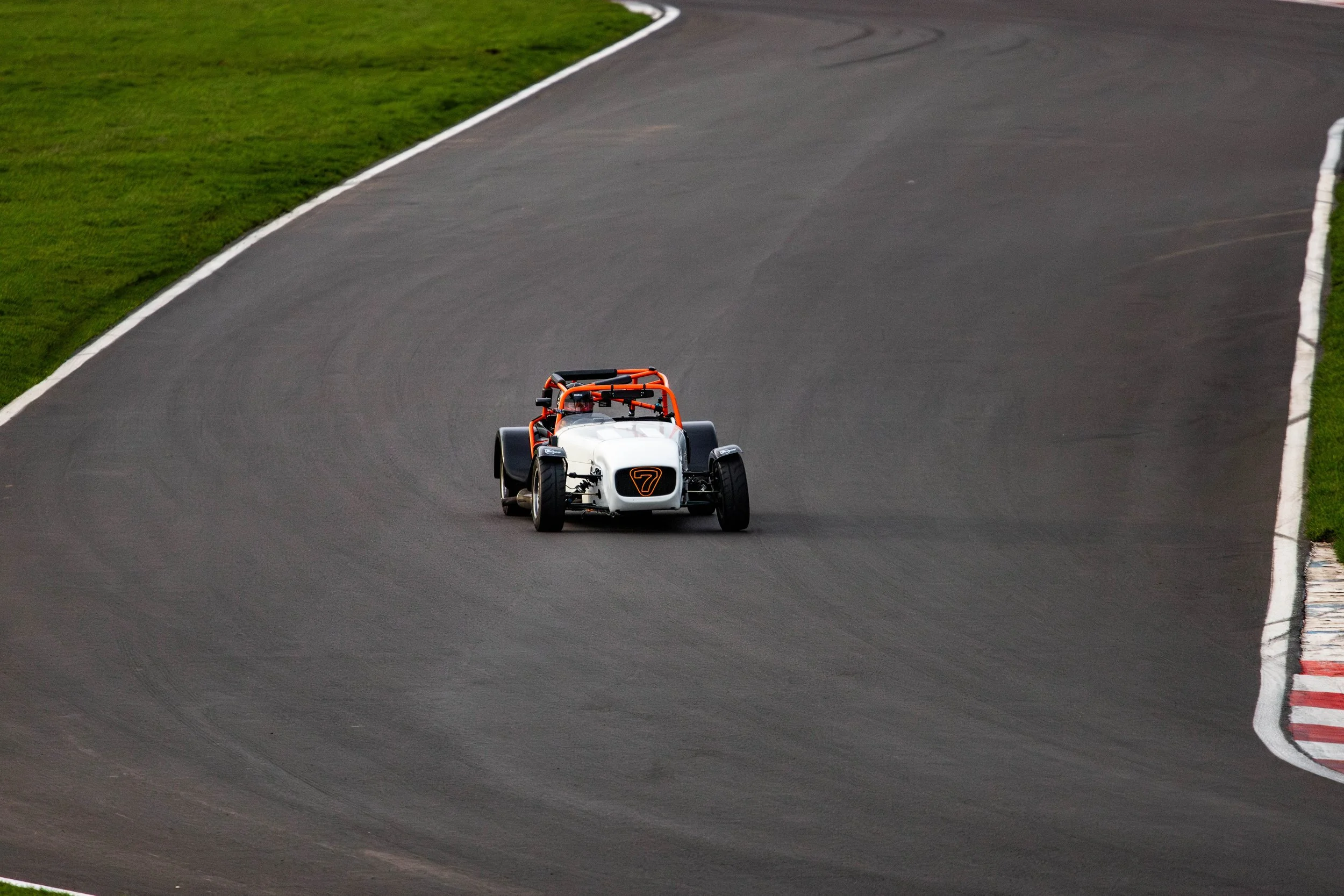 A Caterham race car speeding on a racetrack surrounded by green grass and white curbs.