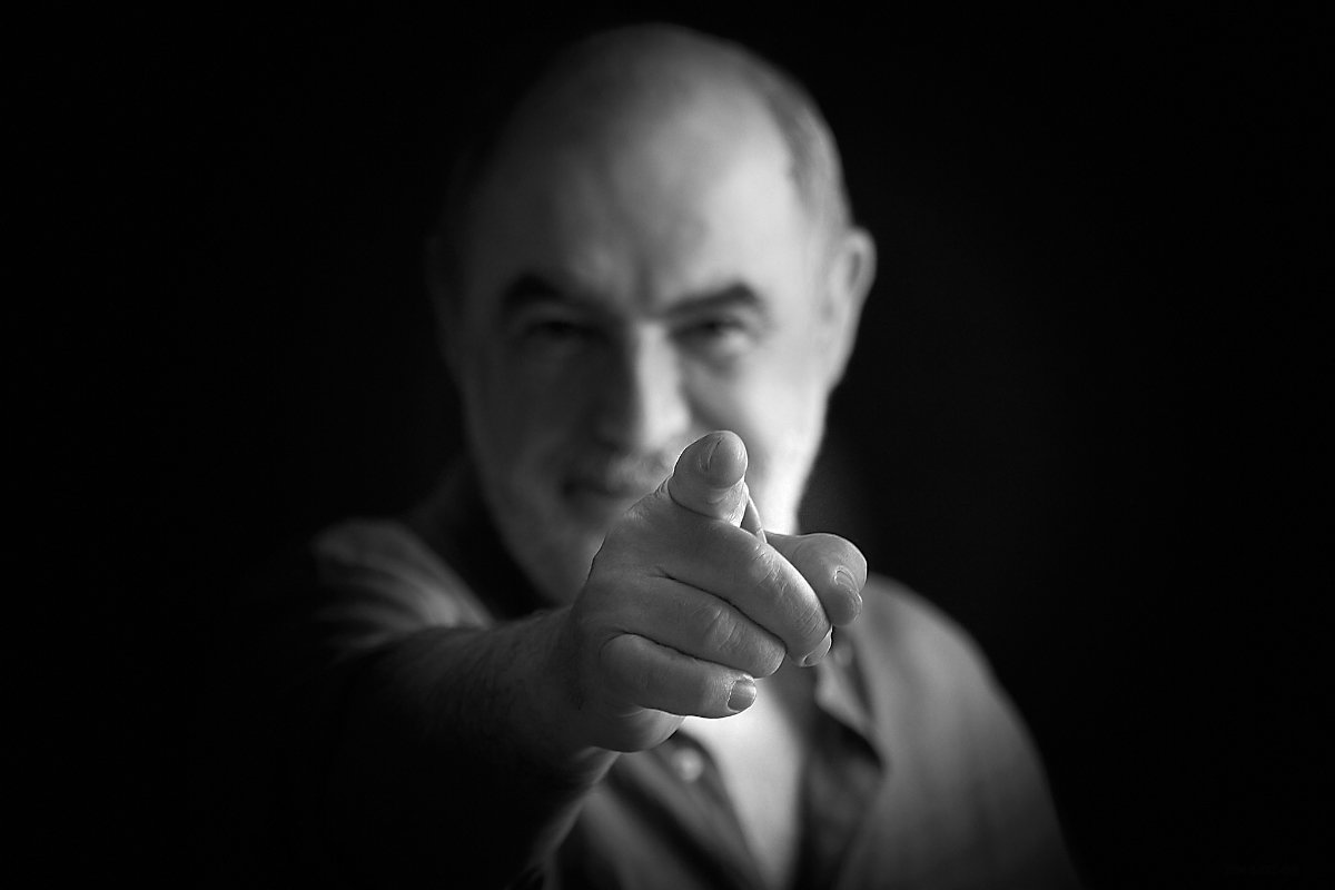Black-and-white photo of a man smiling and pointing directly at the camera.