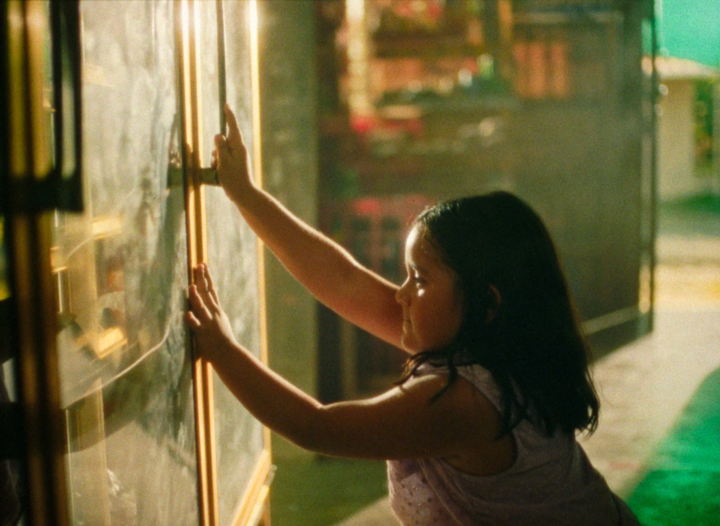 A young girl reaching out to open a drink fridge, with shelves in the background.