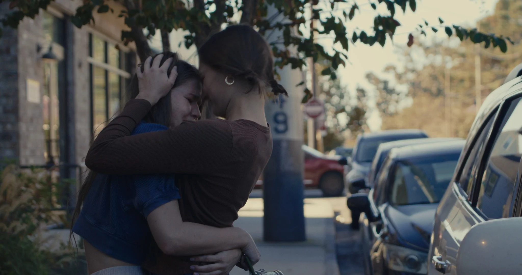 Two women embrace on a city sidewalk, holding each other in a comforting hug.
