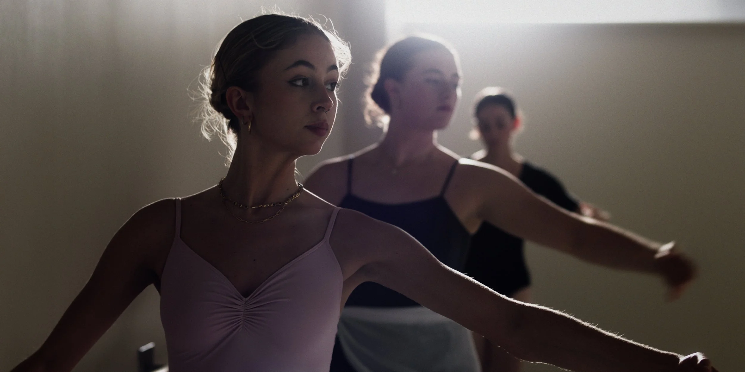 Three women practicing ballet in a dance studio, silhouetted against a backlight.