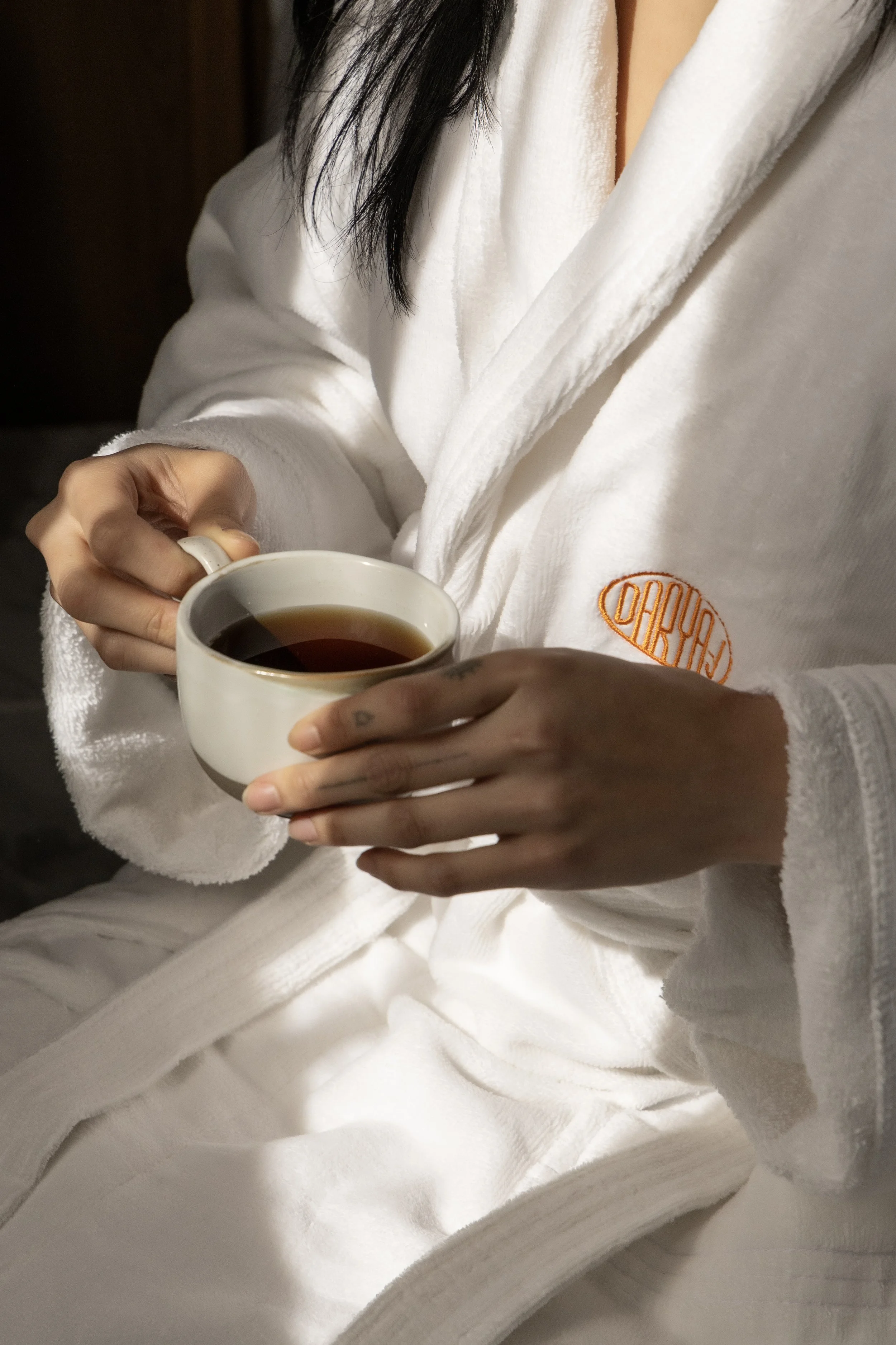 Person in a white bathrobe holding a cup of coffee.