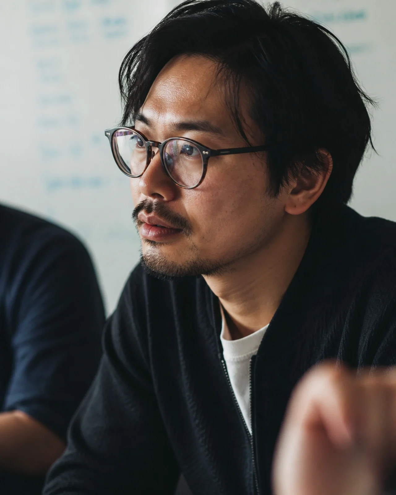 A close-up of a software engineer's focused, calm face during a quiet team discussion, captured in a grainy, cinematic documentary style.