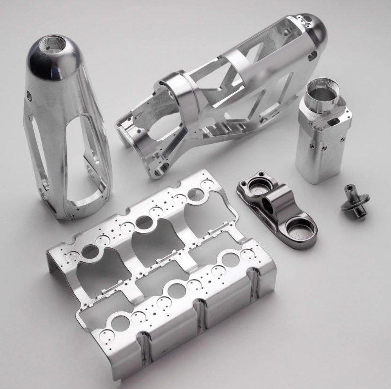 Collection of machined metallic parts and components, possibly for an engine or precision machinery, laid out on a flat surface.