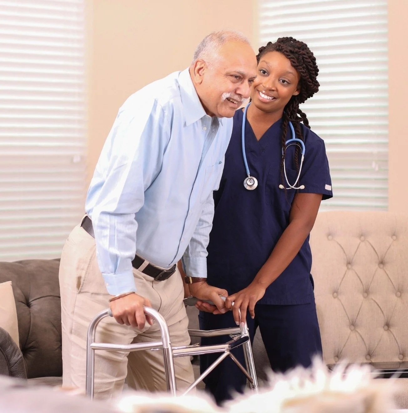 An elderly man with a walker being assisted by a young female nurse or healthcare worker in a patient room.