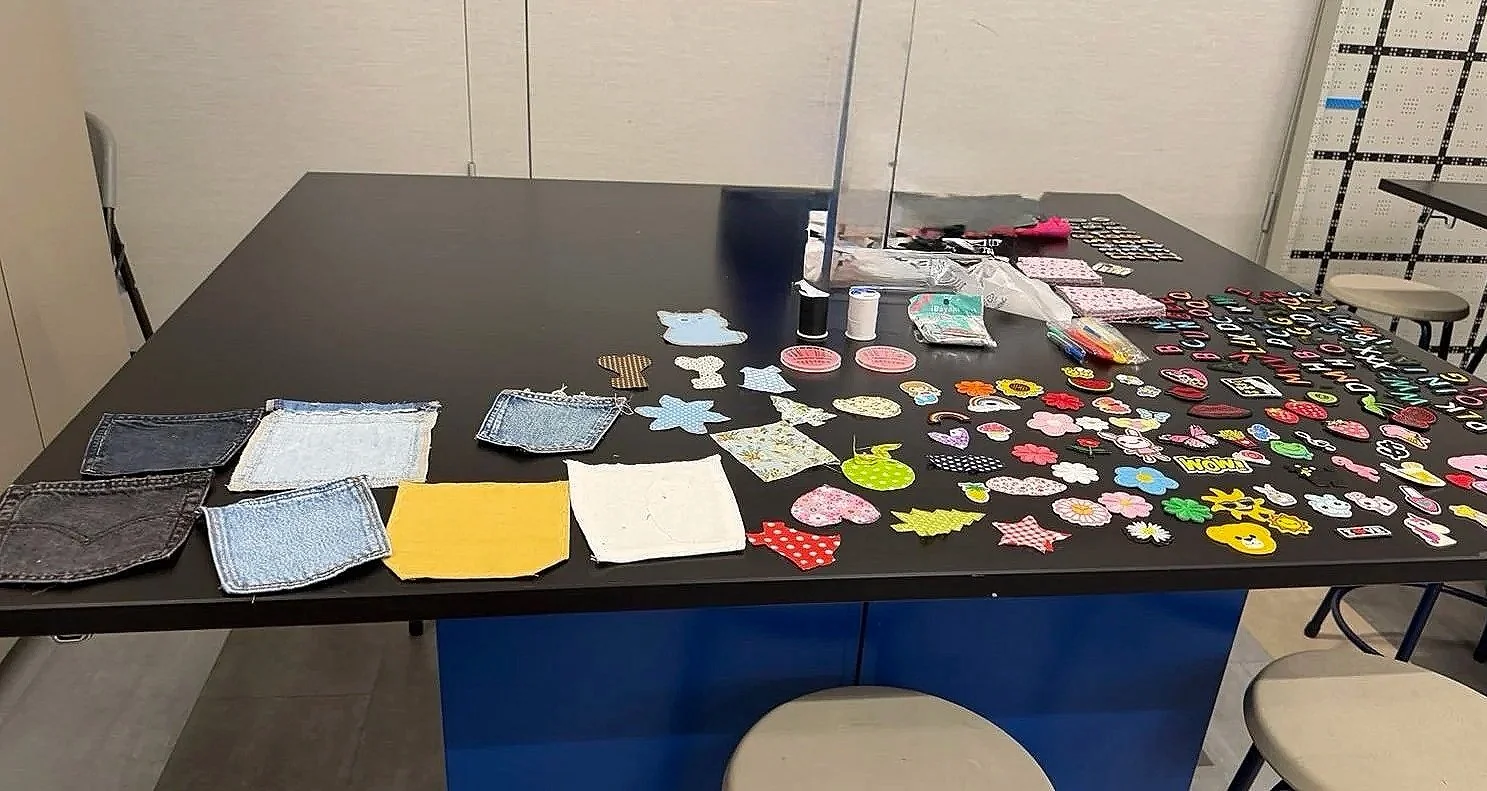 Upcycling workshop table laid out with denim patches, colorful fabric scraps, embroidered stickers, and sewing supplies