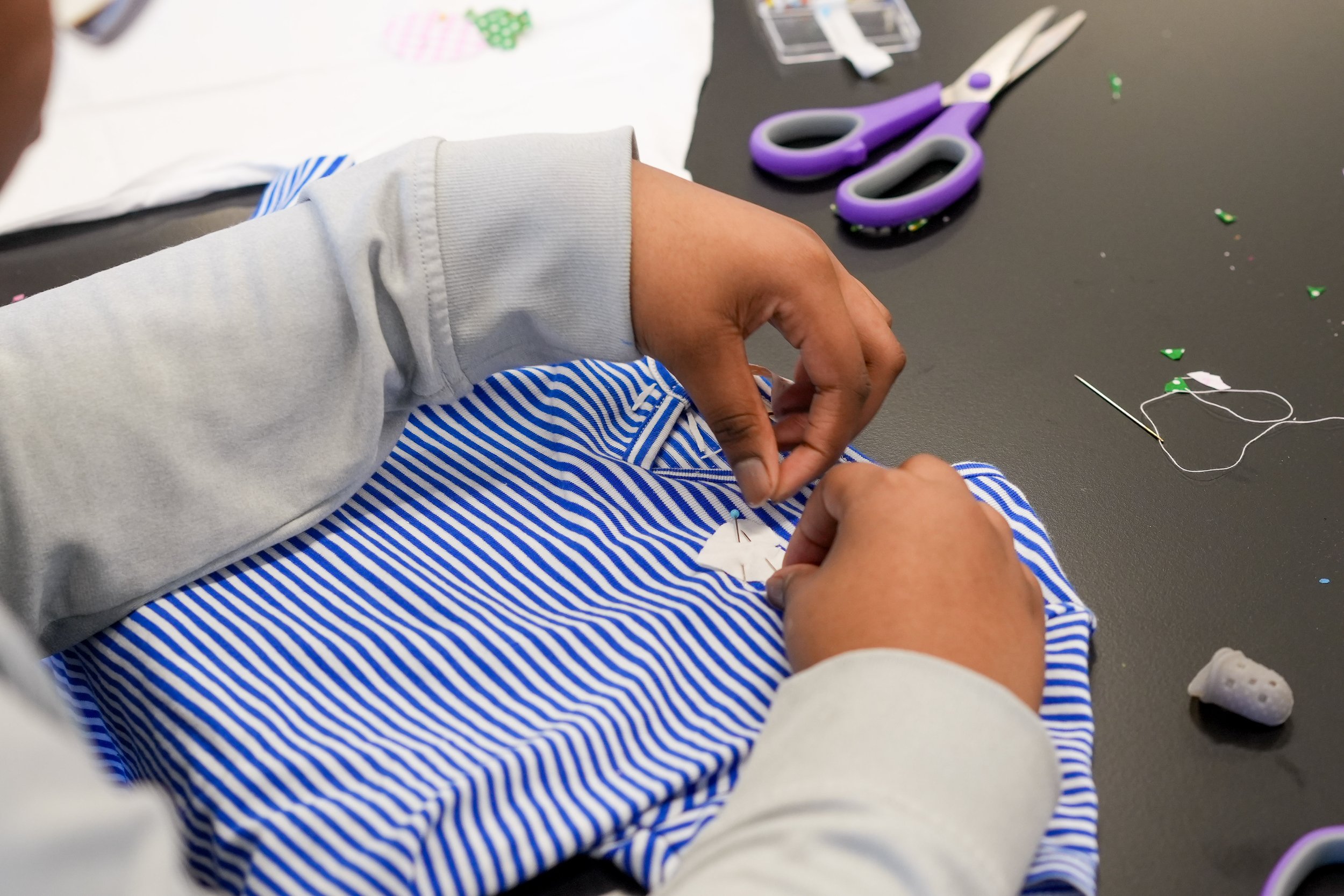 Close-up of hands pinning and hand-sewing a blue and white striped fabric piece during an upcycling workshop
