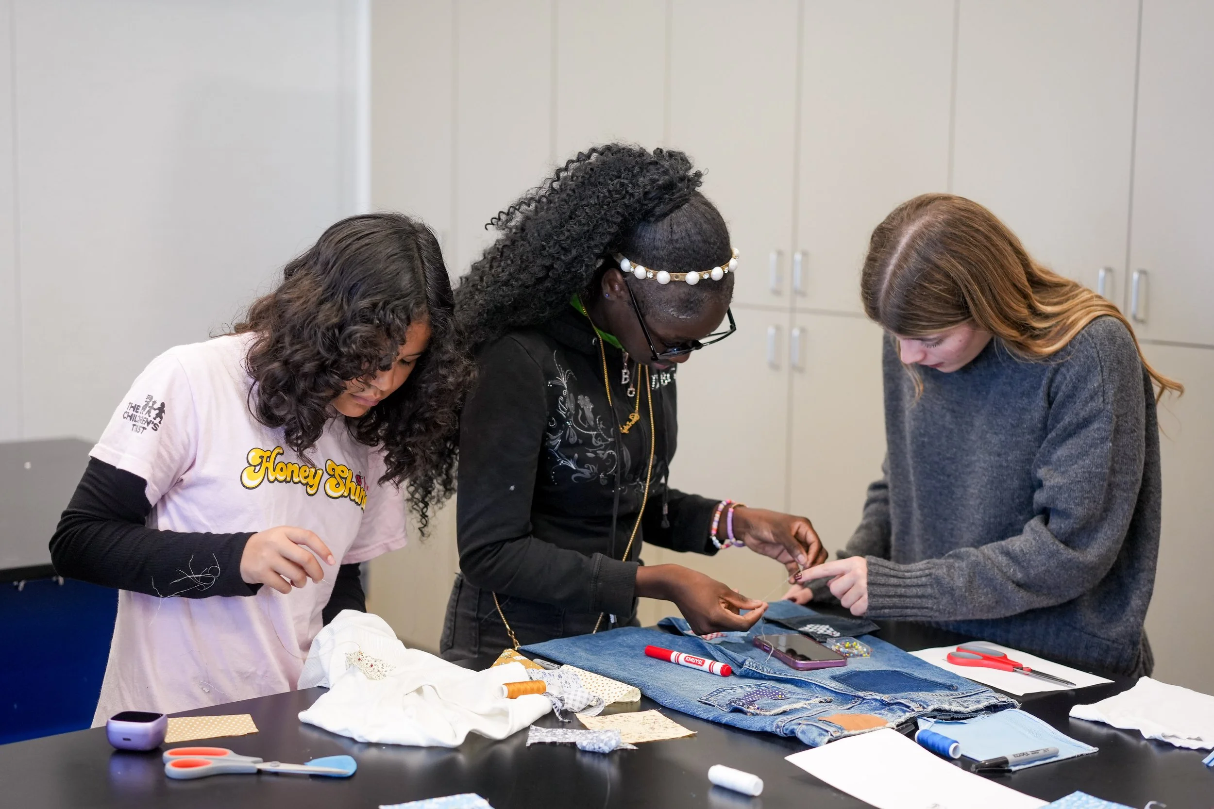 Two girls working together on upcycling denim jeans and fabric patches during a hands-on sewing workshop