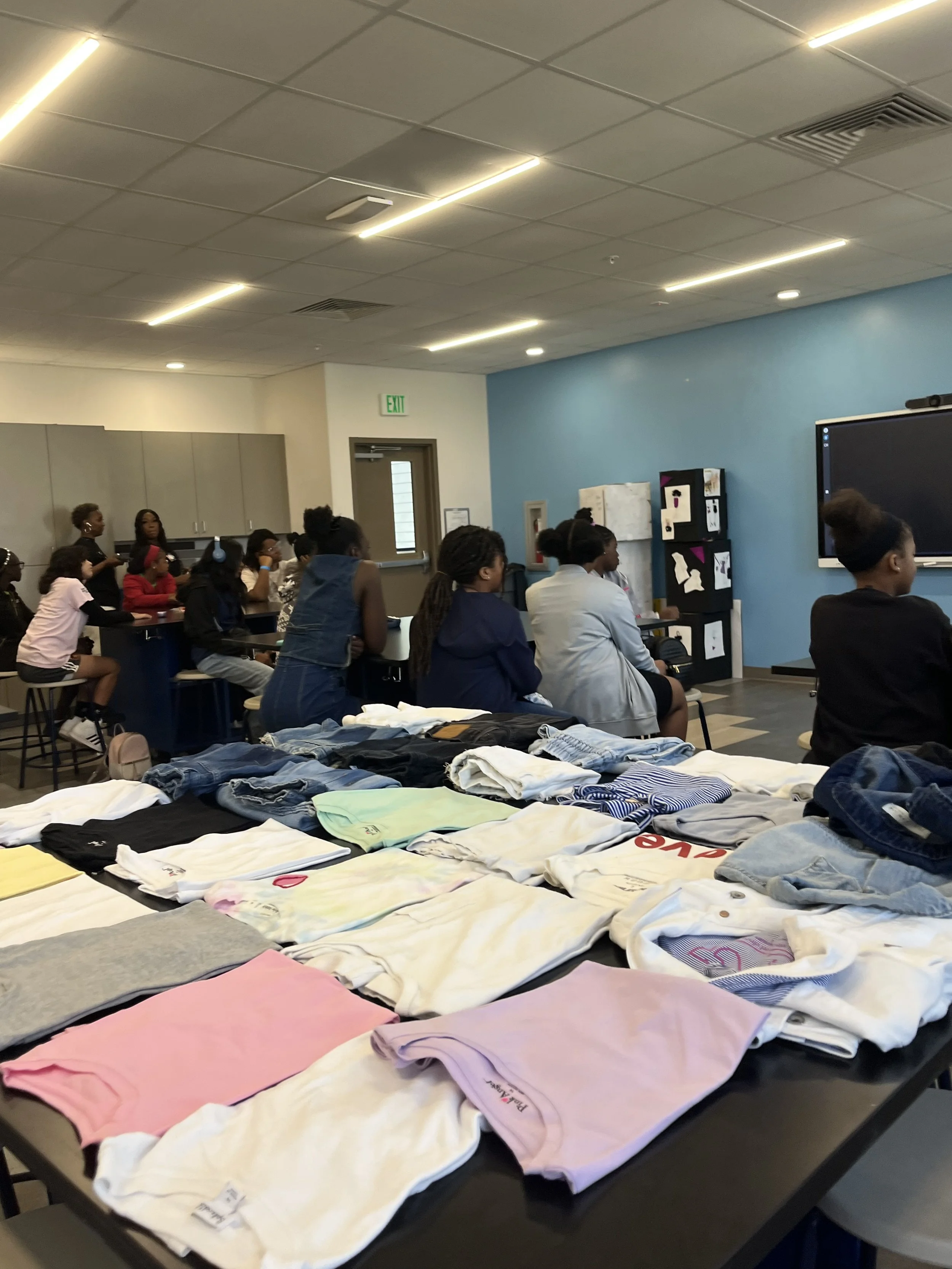 Folded clothing donations spread across a table at a Thread by Thread community clothing drive event