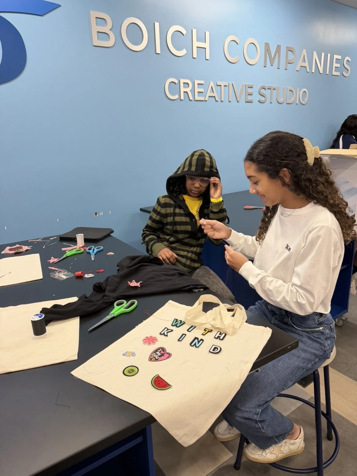Two girls working on upcycled tote bags with patches and embellishments at a Thread by Thread workshop