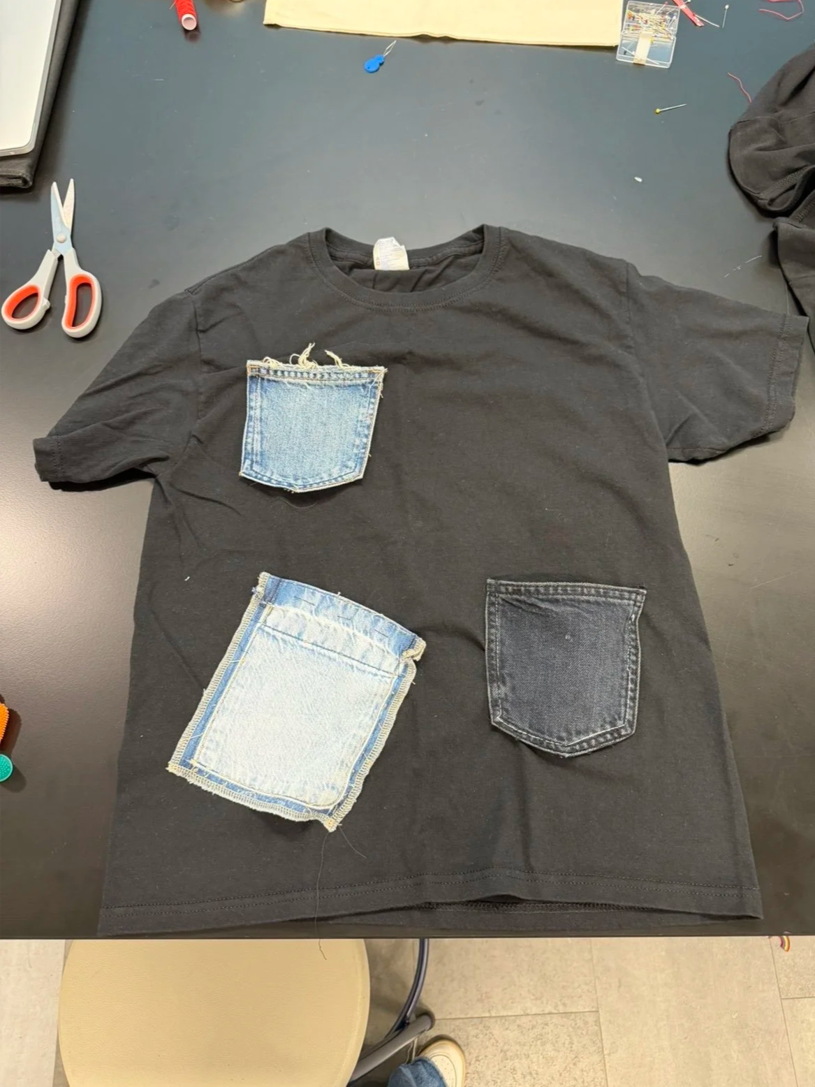 Black t-shirt upcycled with denim pocket patches, a finished piece from a Thread by Thread workshop