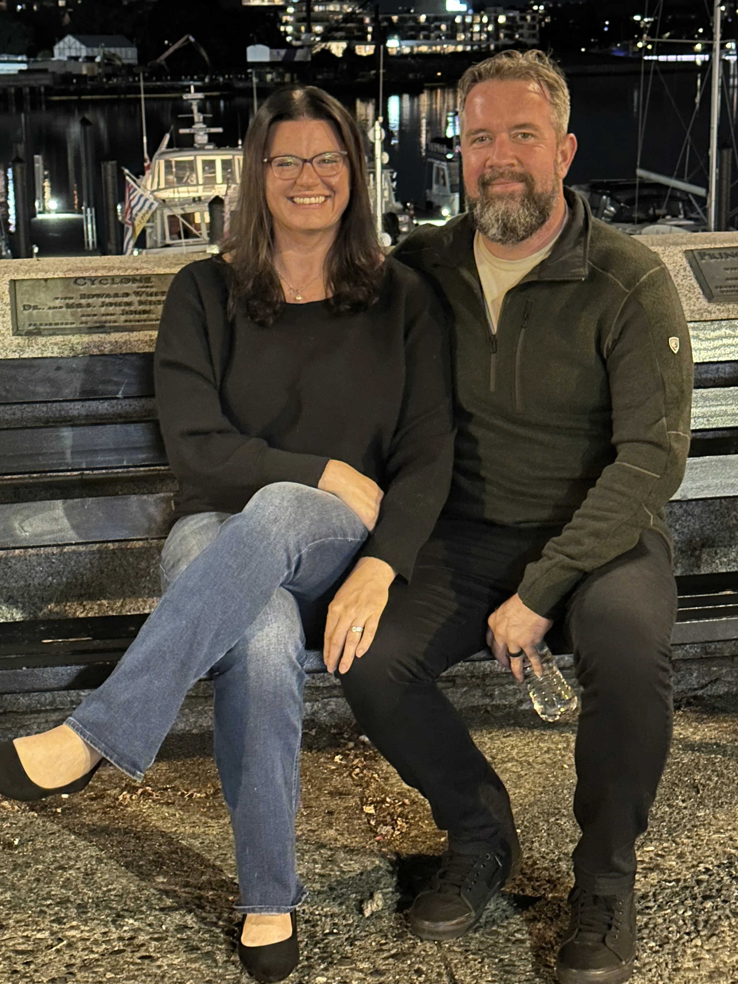 Couple sitting together on a bench at a marina in the evening