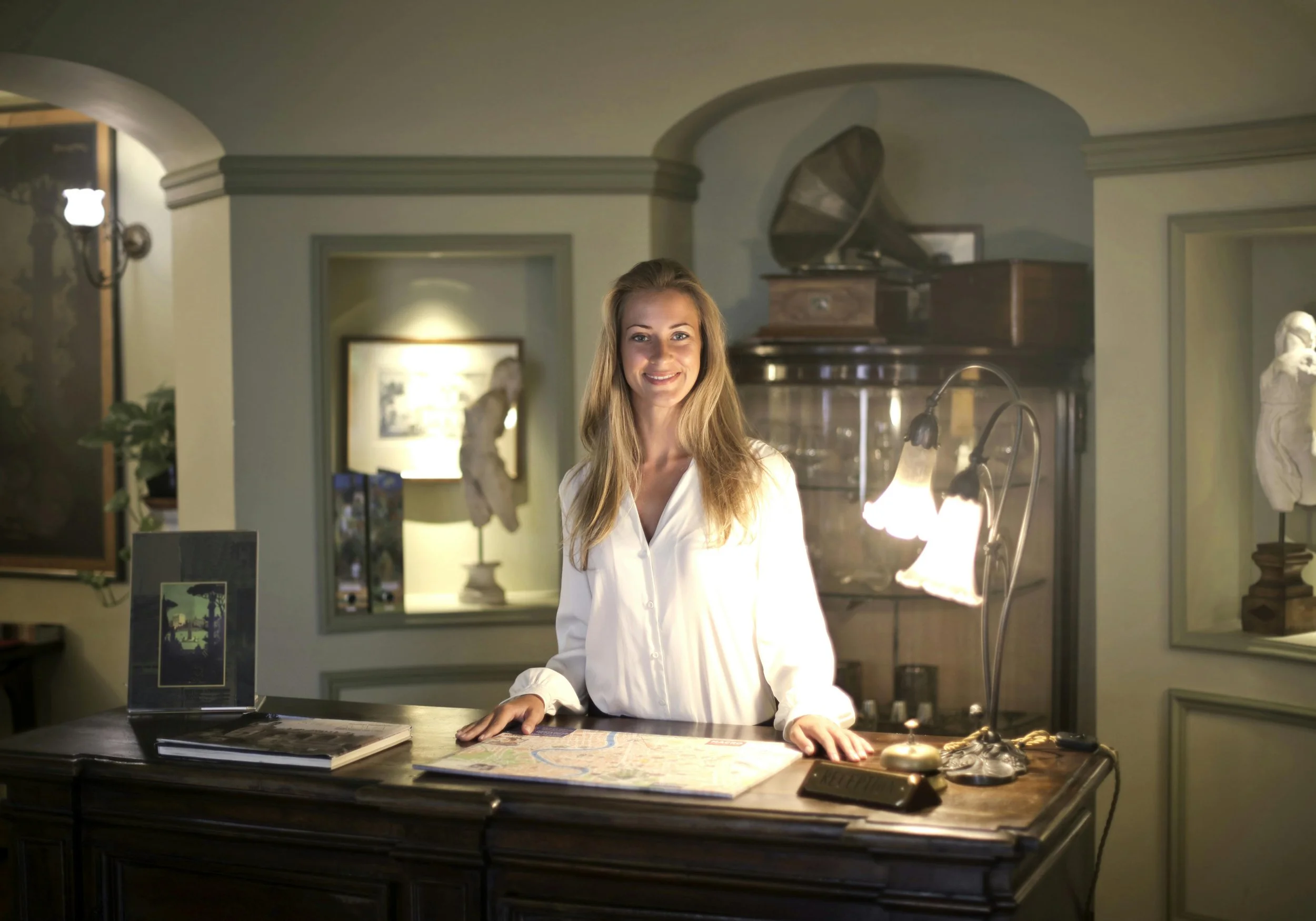 Friendly concierge standing behind a reception desk inside a luxury hotel, ready to assist guests with information and services.