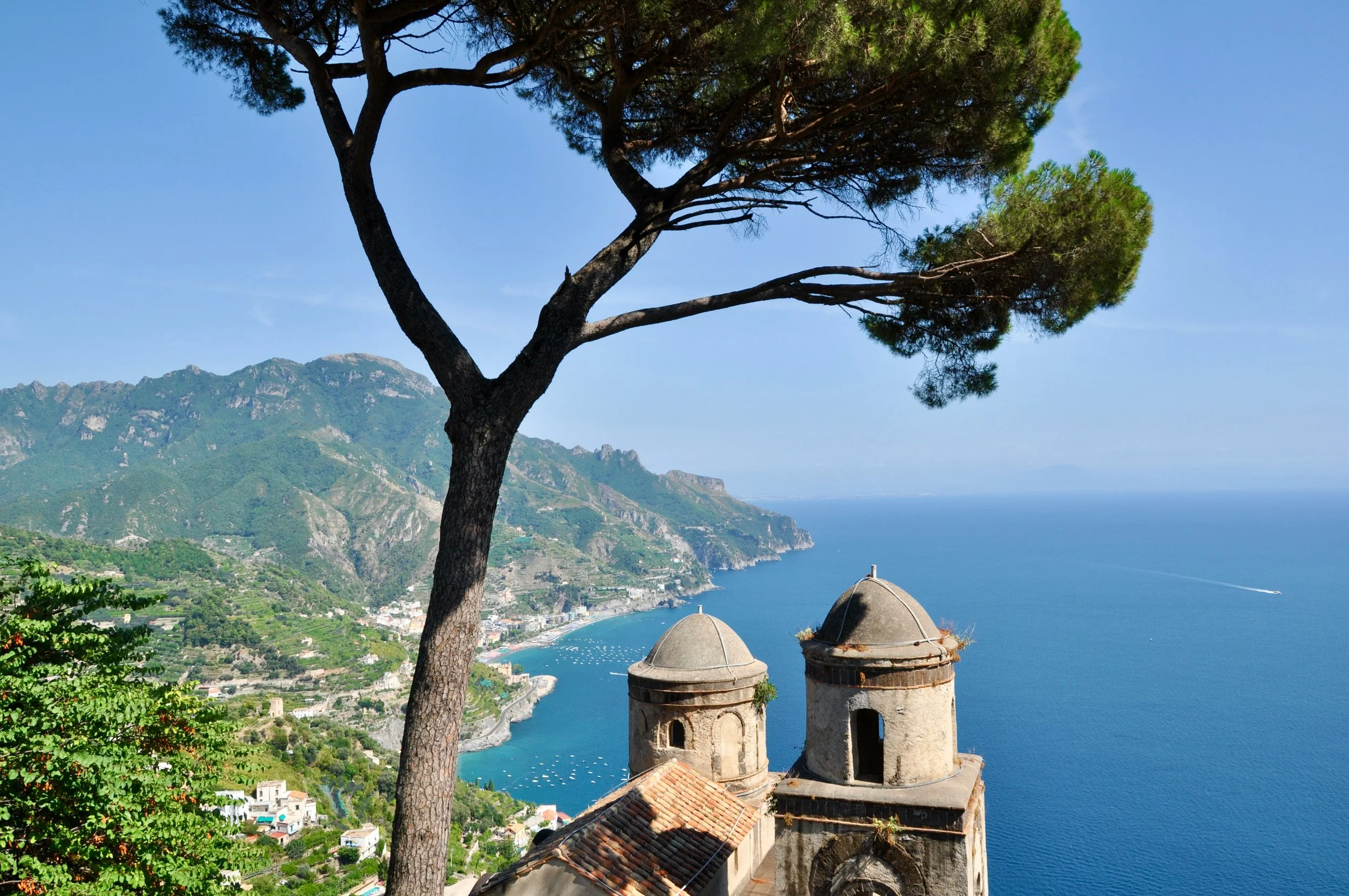 Scenic view from Ravello on Italy’s Amalfi Coast, with a pine tree framing historic church towers overlooking the blue Mediterranean and coastal villages below.