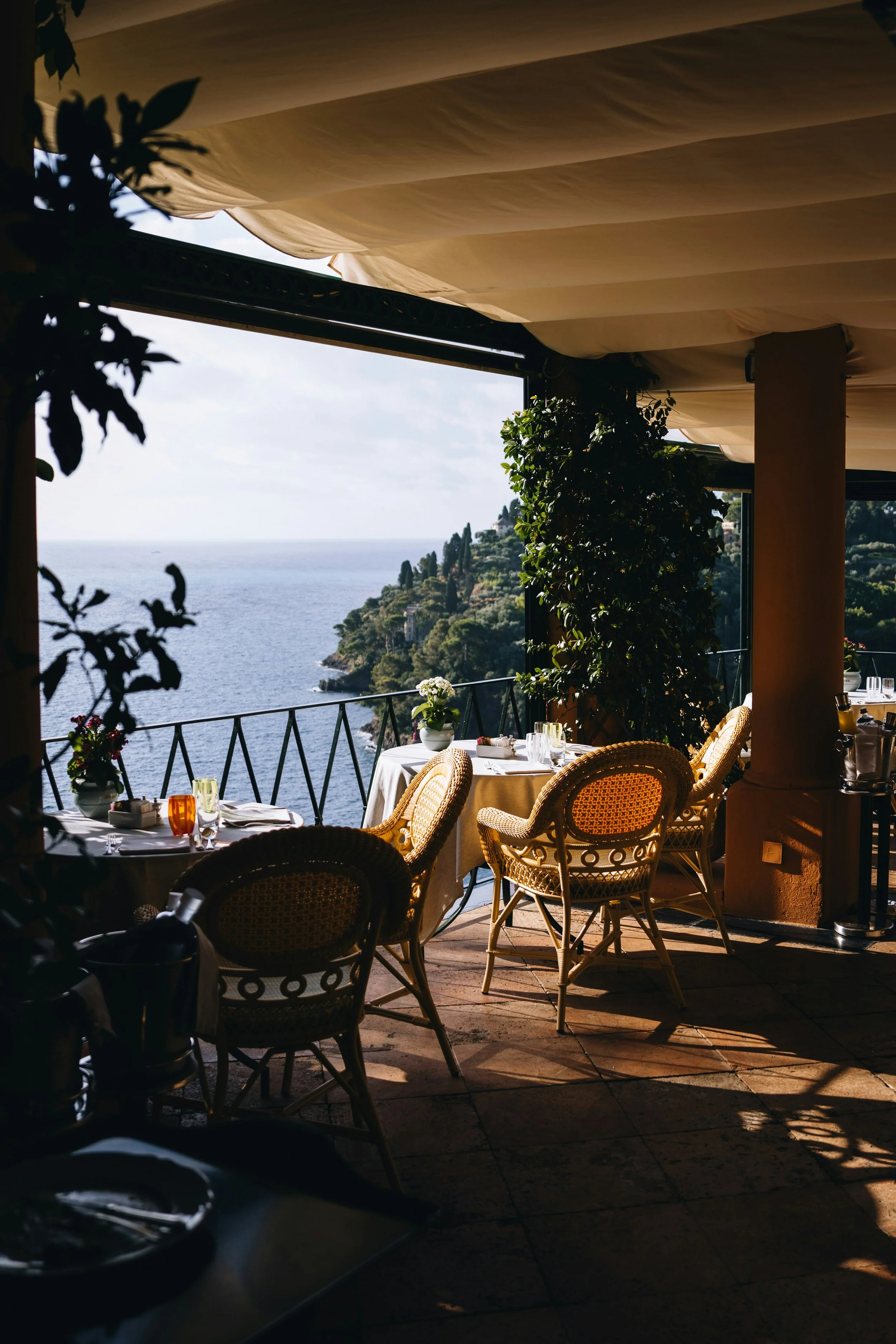 Outdoor restaurant terrace on Italy’s Amalfi Coast with wicker chairs, white tablecloths, and a shaded view overlooking the Mediterranean Sea.