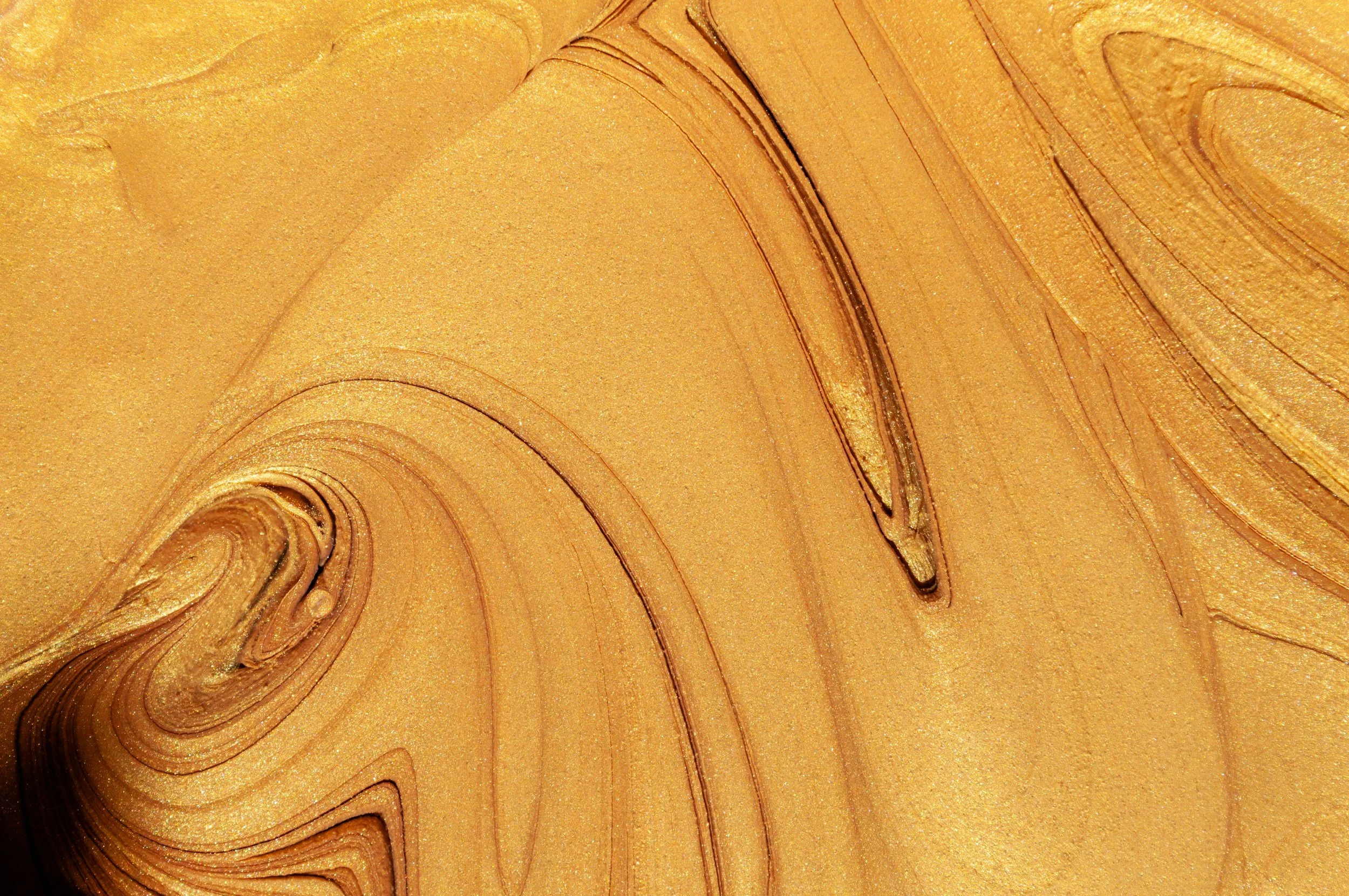 Close-up of a swirling, gold-colored metallic surface with streaks and ripples.