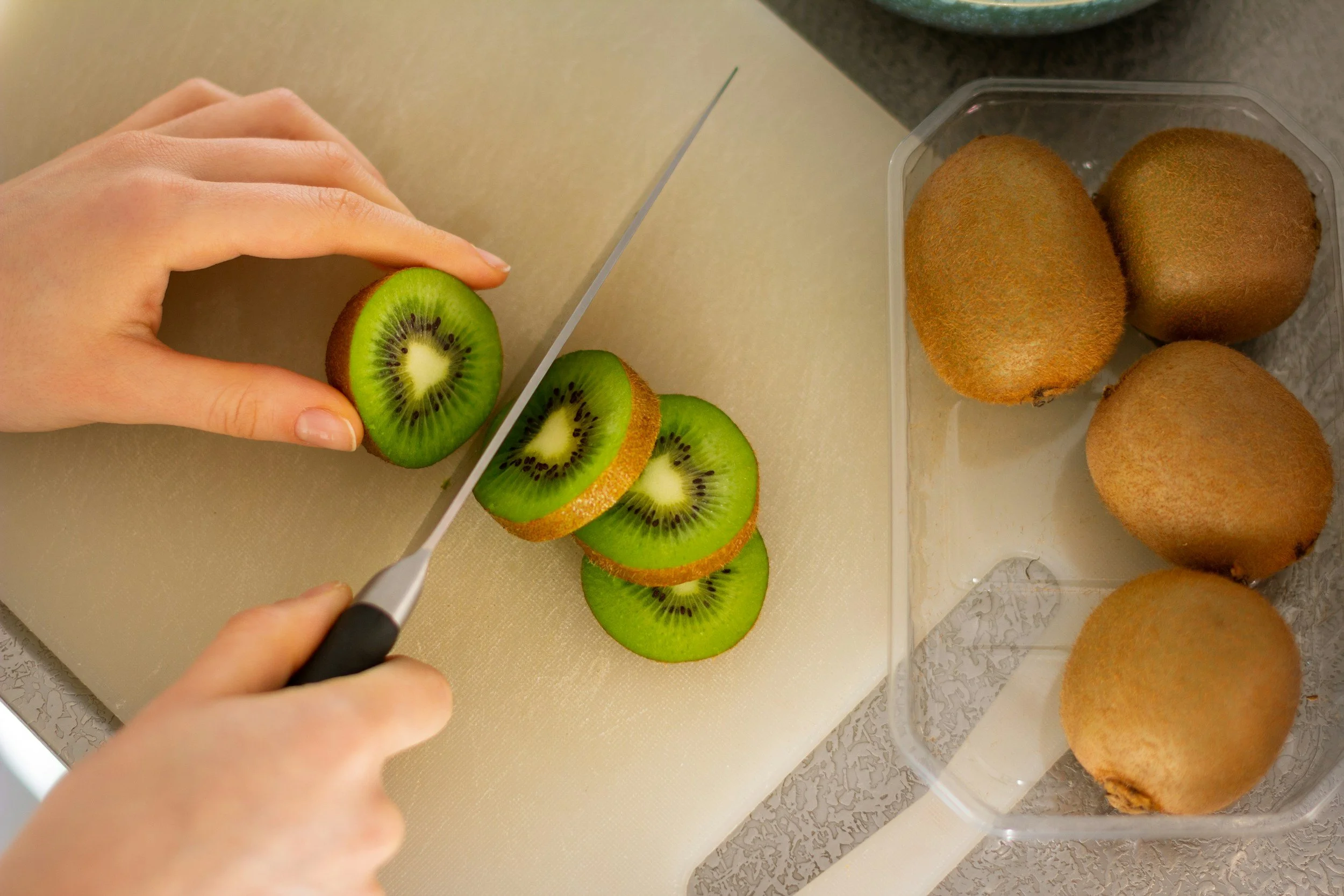 Hands slicing fresh kiwi on a cutting board to represent immune-supporting foods