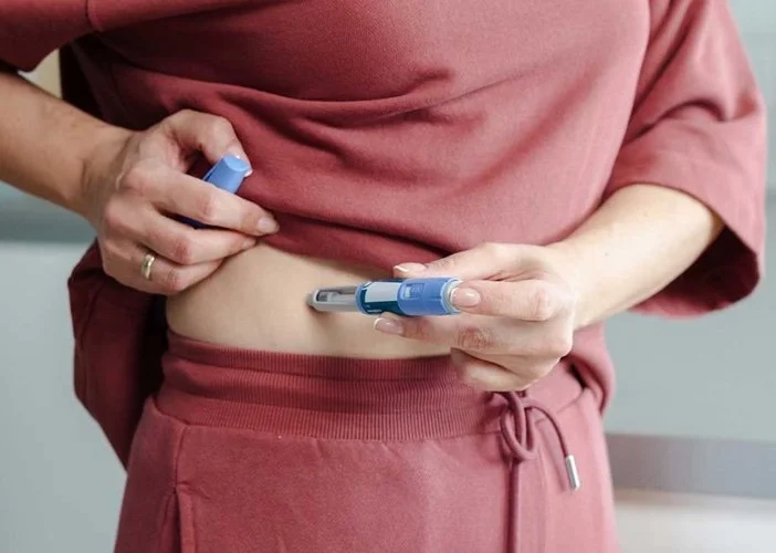 Person administering a GLP-1 injection into the abdomen at home.