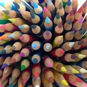 Close-up of many colored pencils arranged with tips pointing outward.