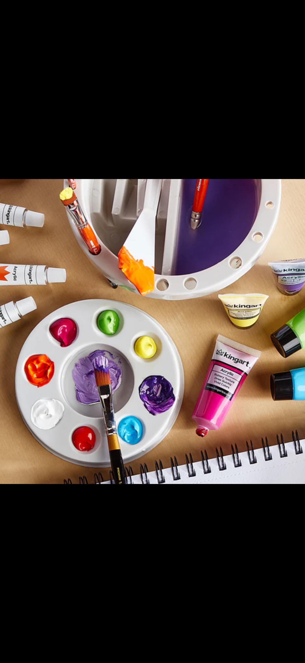 Assorted acrylic paint tubes and a palette with various colored paints on a wooden surface.