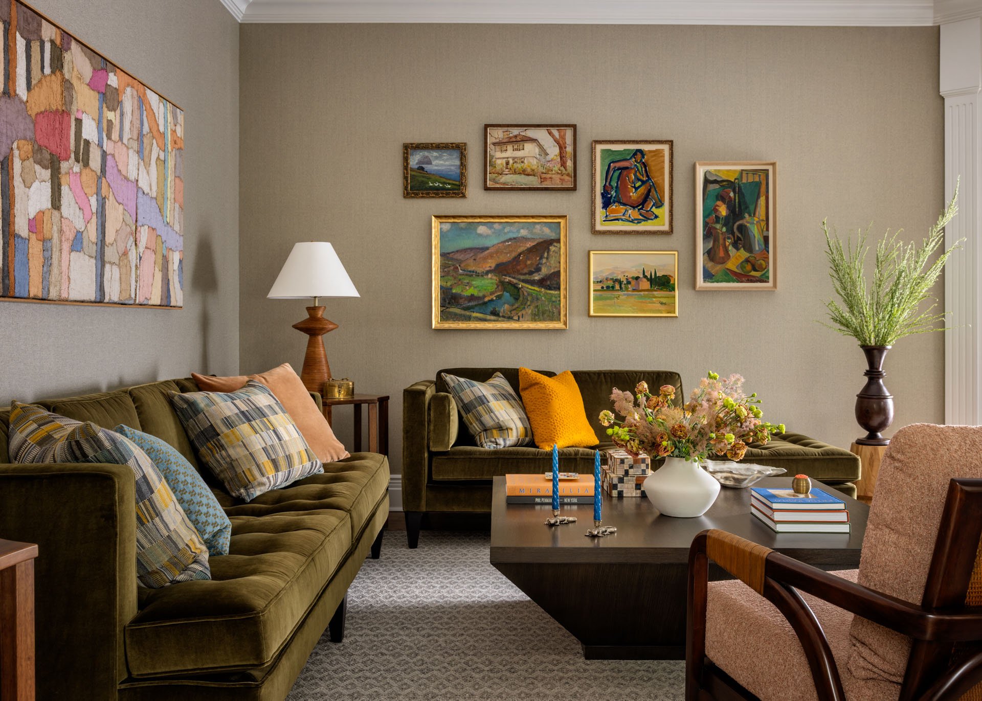 Living room with two green sofas, a coffee table with books and a vase of flowers, wall art, and a beige armchair.