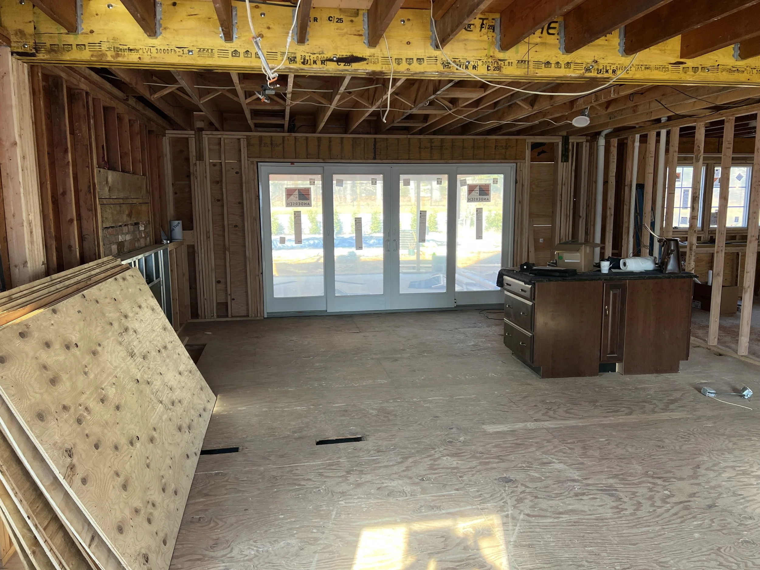 Interior of a house under construction with exposed wooden framing, a sliding glass door, and a small kitchen island.