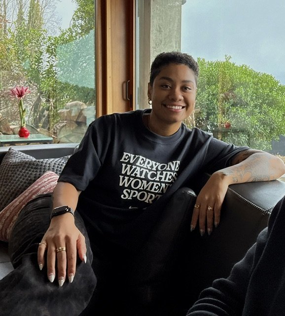 Bri wearing a black tshirt, resting her left arm on a couch she is sitting on