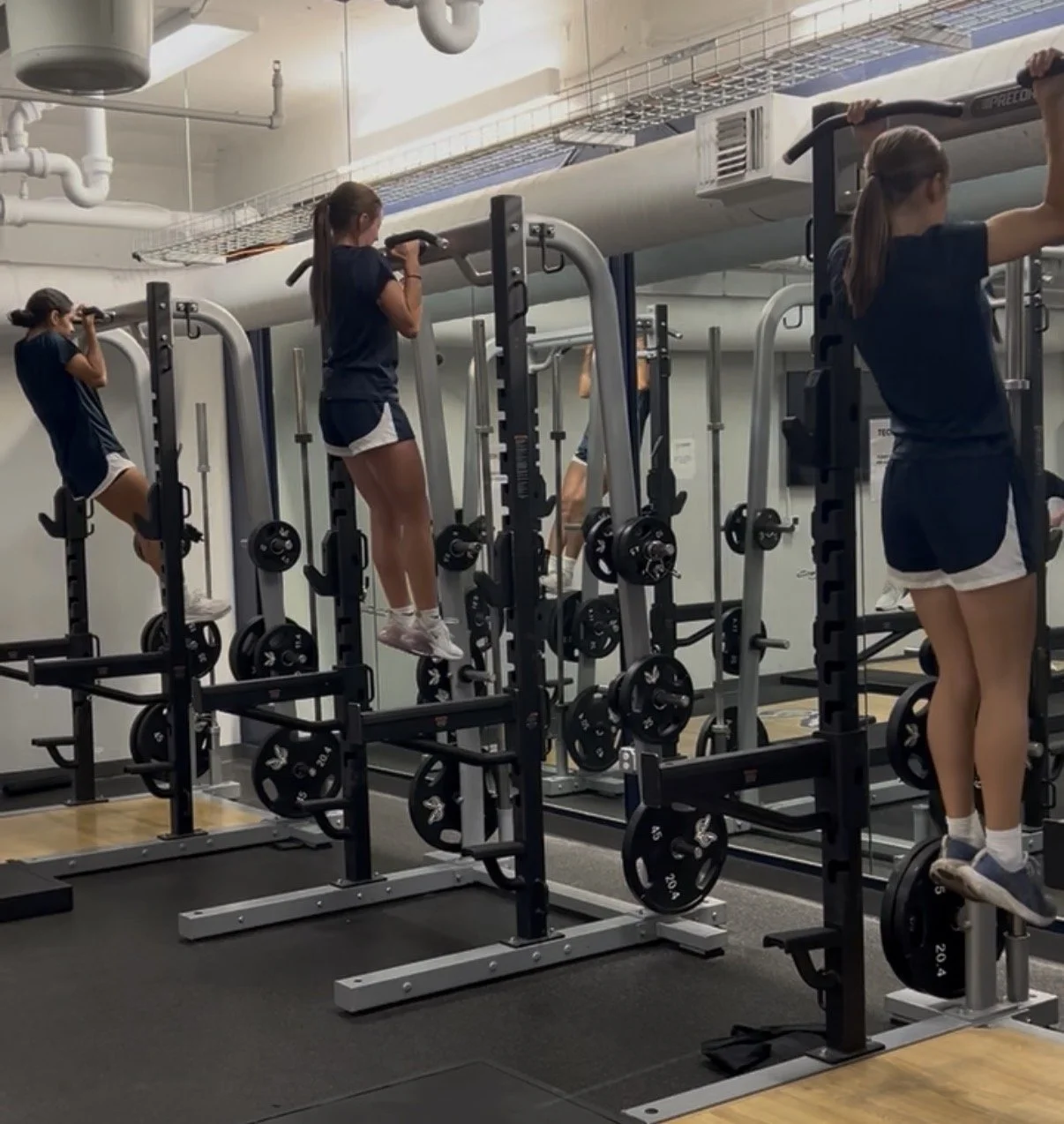 Four girls lifting their knees on exercise equipment in a gym.