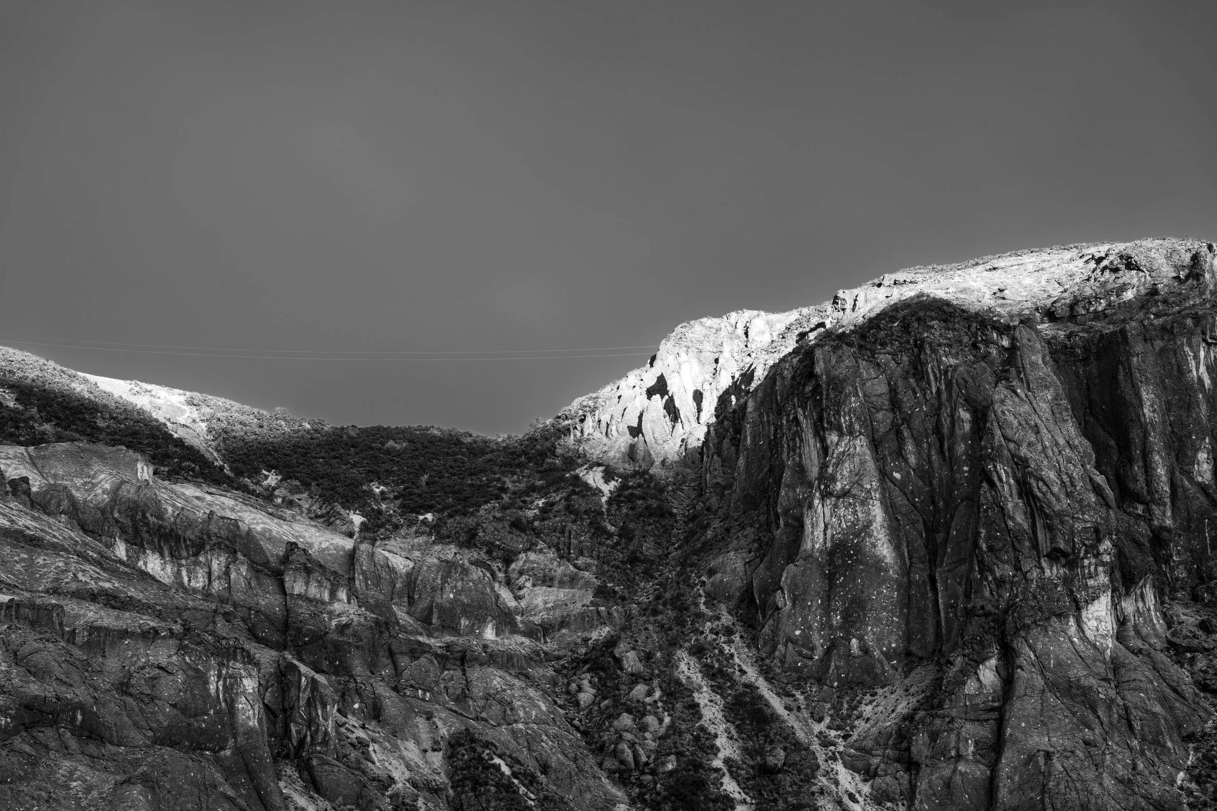 Black and white photograph of a mountainous landscape with rocky cliffs and sparse vegetation.
