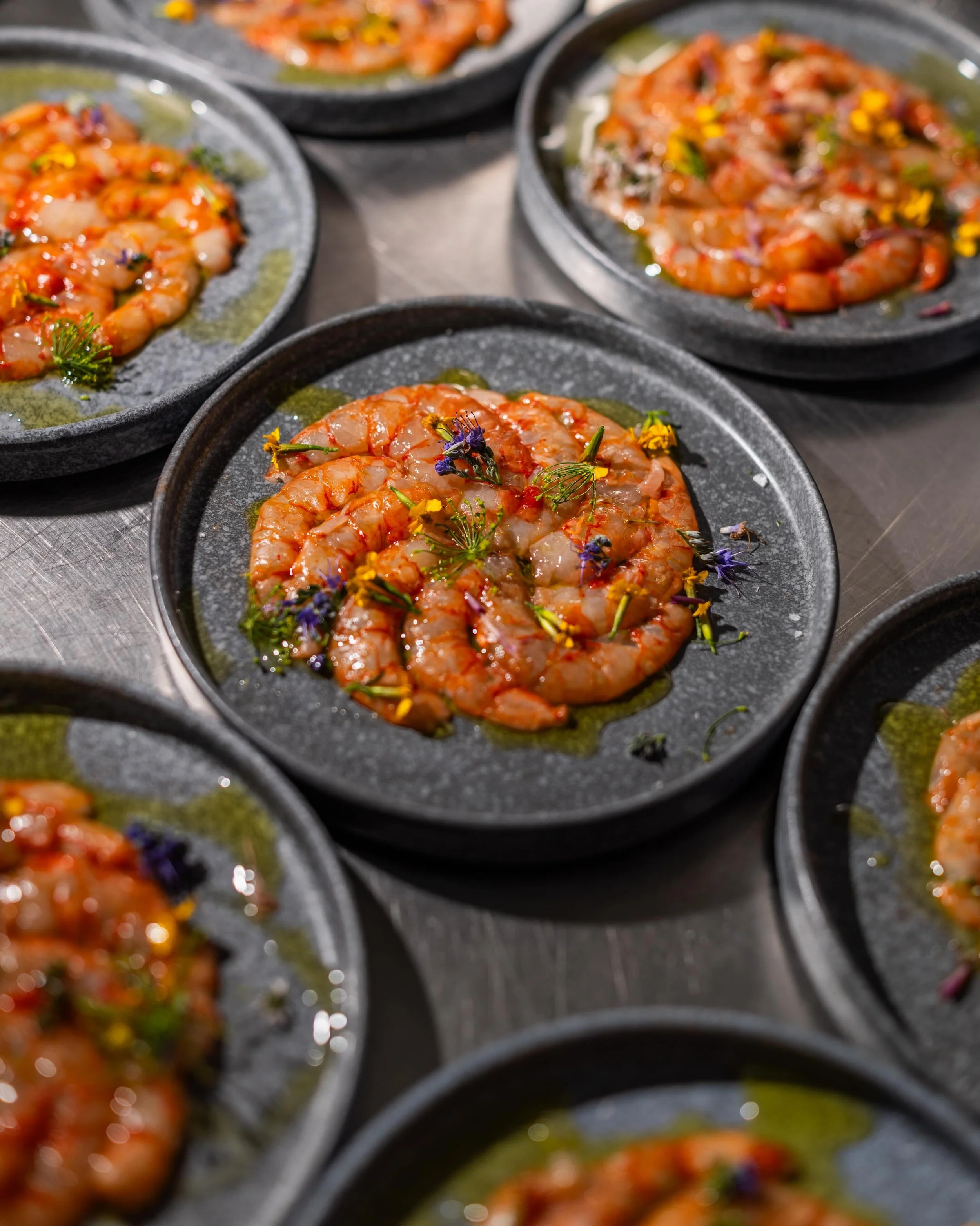 Plate of raw shrimp garnished with herbs and edible flowers.