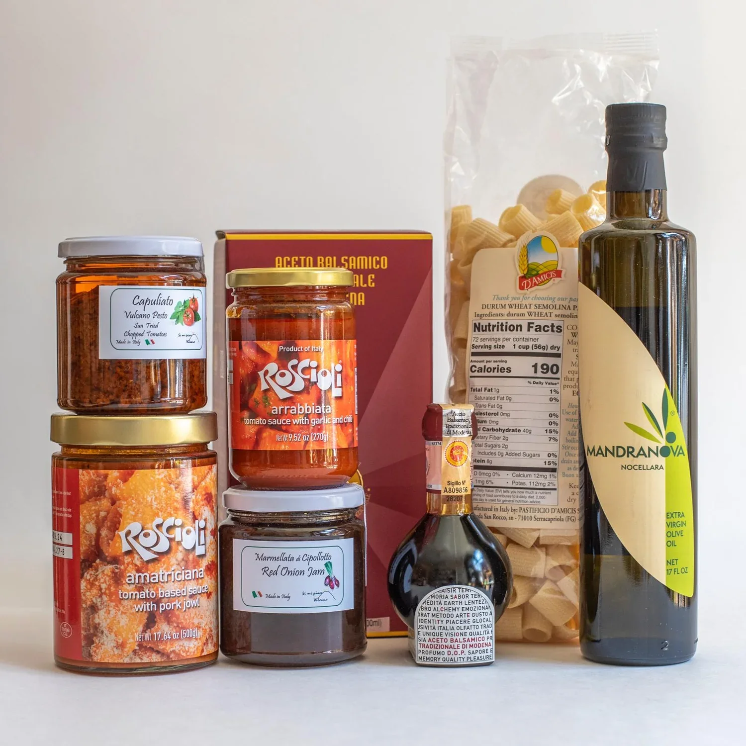 Assorted Italian food products including jars of tomato sauce, a box of balsamic vinegar, a bag of wheat semolina pasta, a bottle of extra virgin olive oil, and a small bottle of balsamic vinegar.
