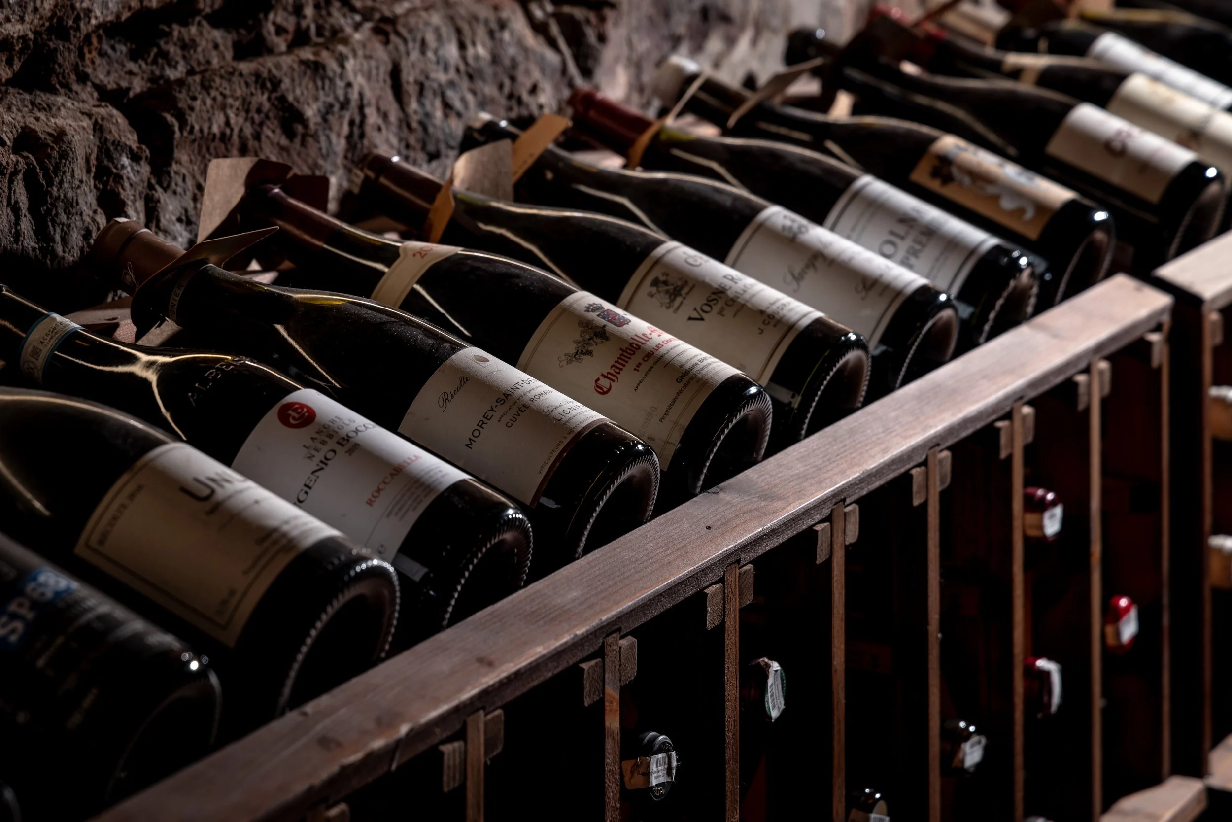 Multiple bottles of red wine stored horizontally in wooden wine racks in Roscioli's wine cellar