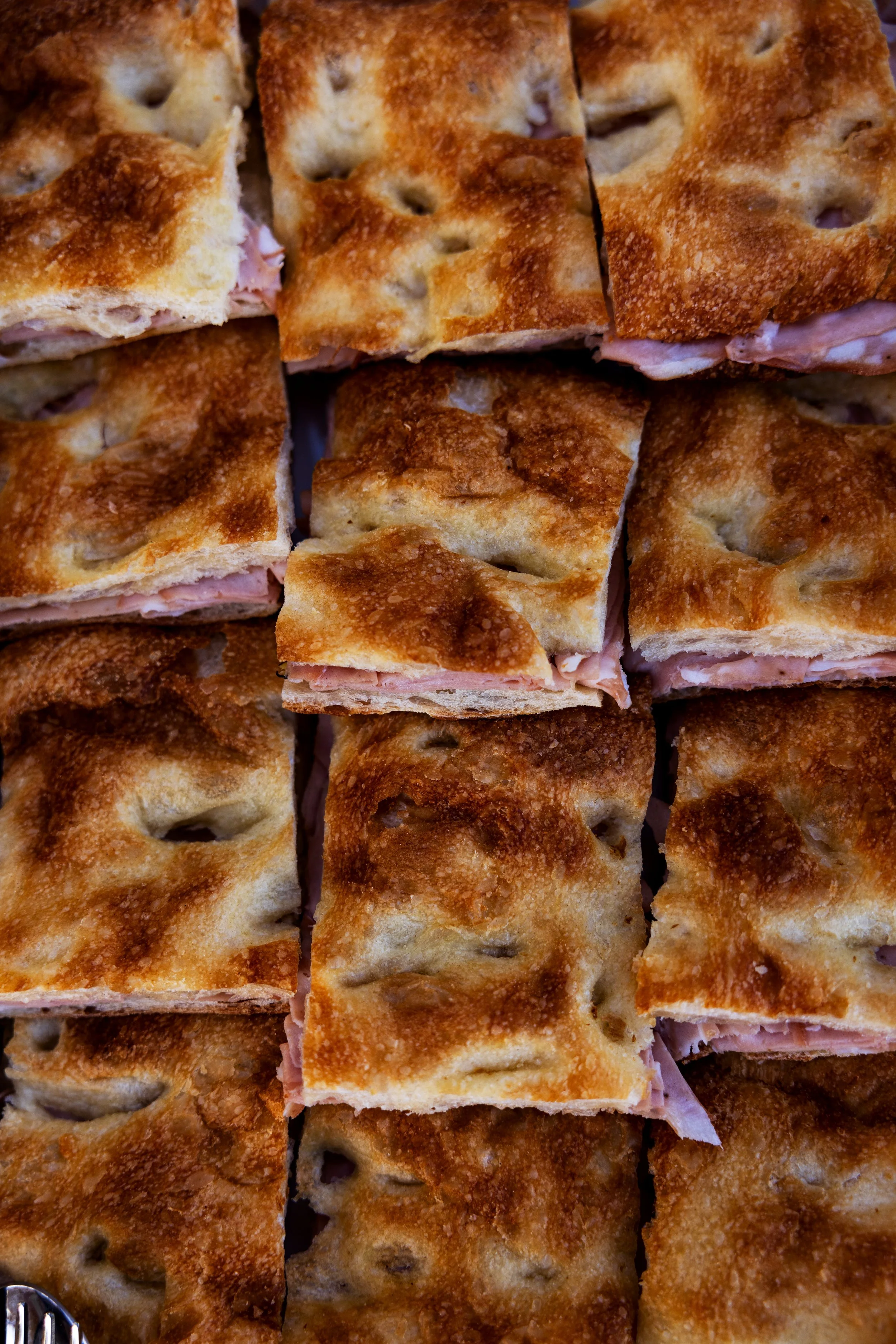 Close-up of baked ham and cheese panini sandwiches cut into squares, showing crispy golden crust and melted cheese inside.