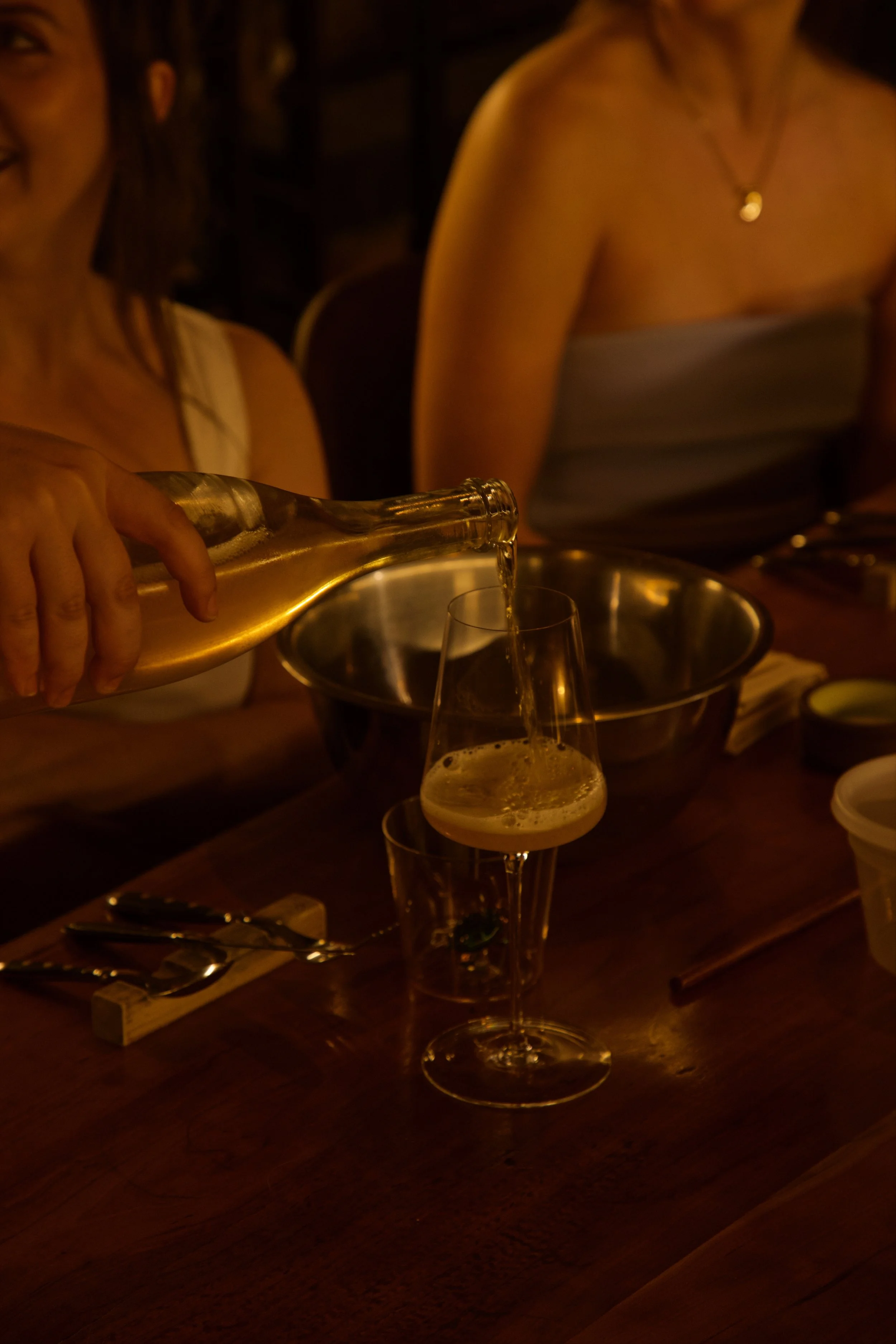People at a dinner table pouring sparkling wine into glasses in the wine cellar at Roscioli NYC