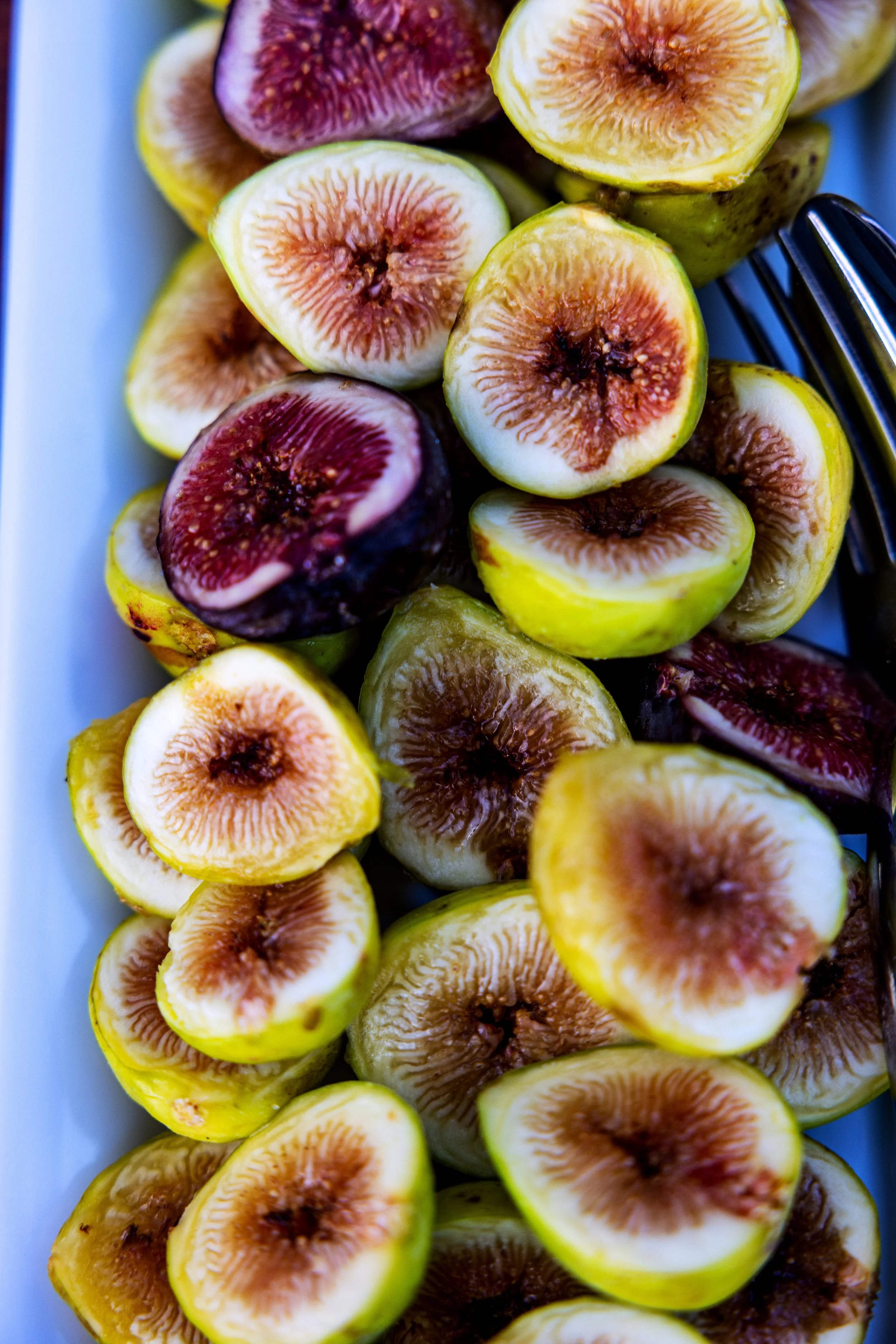 Close-up of halved figs with green and purple skins on a white platter.