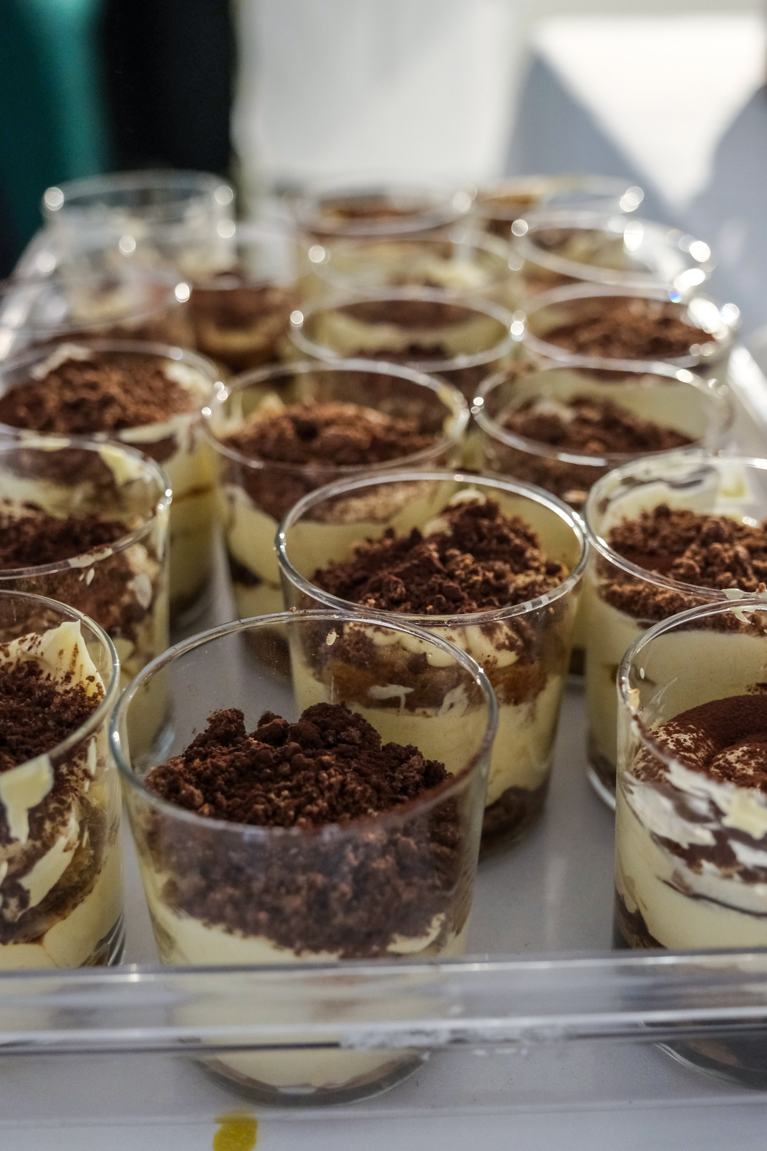 Multiple individual servings of tiramisu in clear cups topped with cocoa powder.