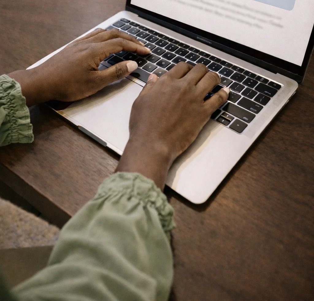 Person typing on a laptop keyboard with a wooden desk surface.