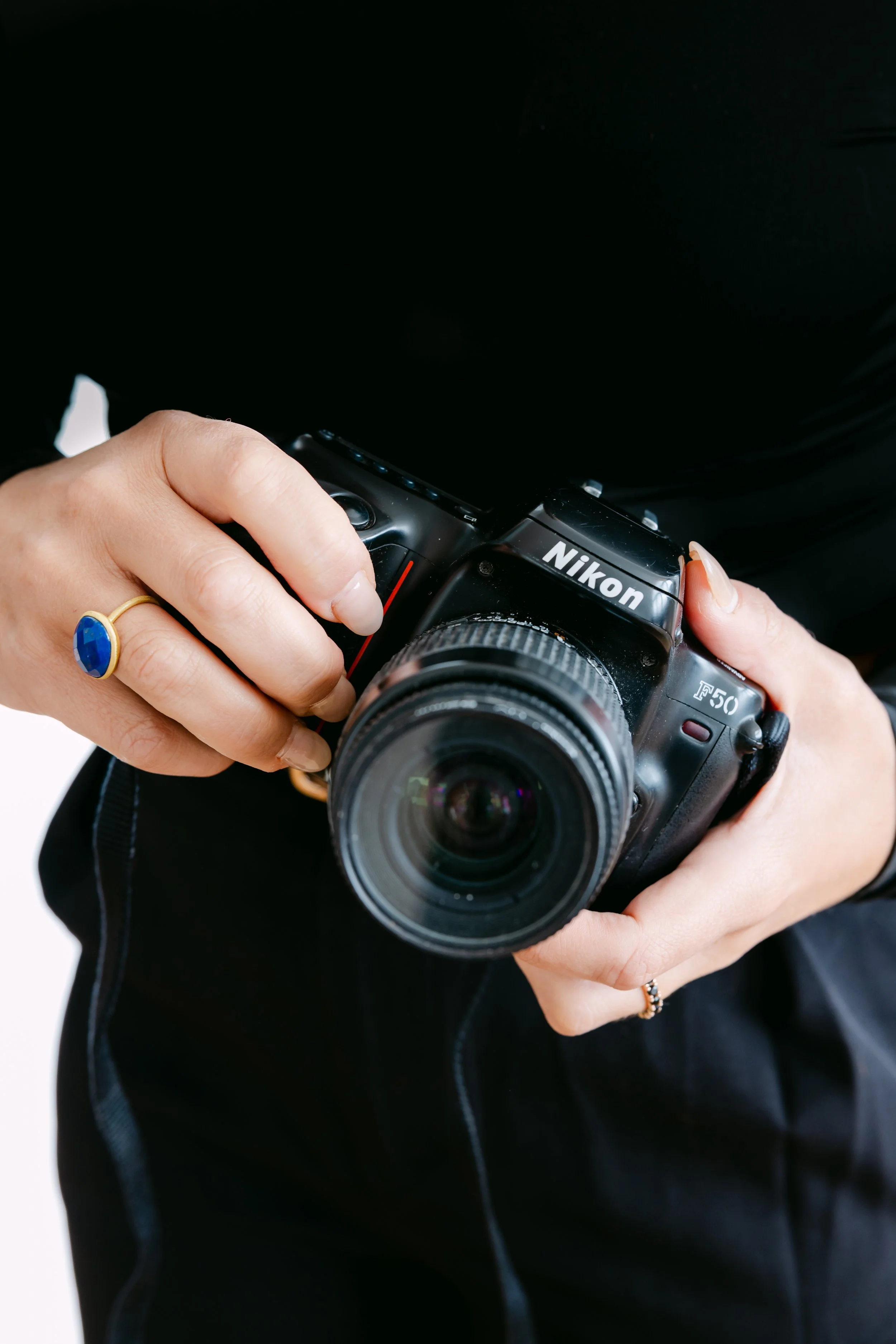 A woman wearing a black off-the-shoulder top with a brown belt taking a mirror selfie with a smartphone featuring a leopard print case.