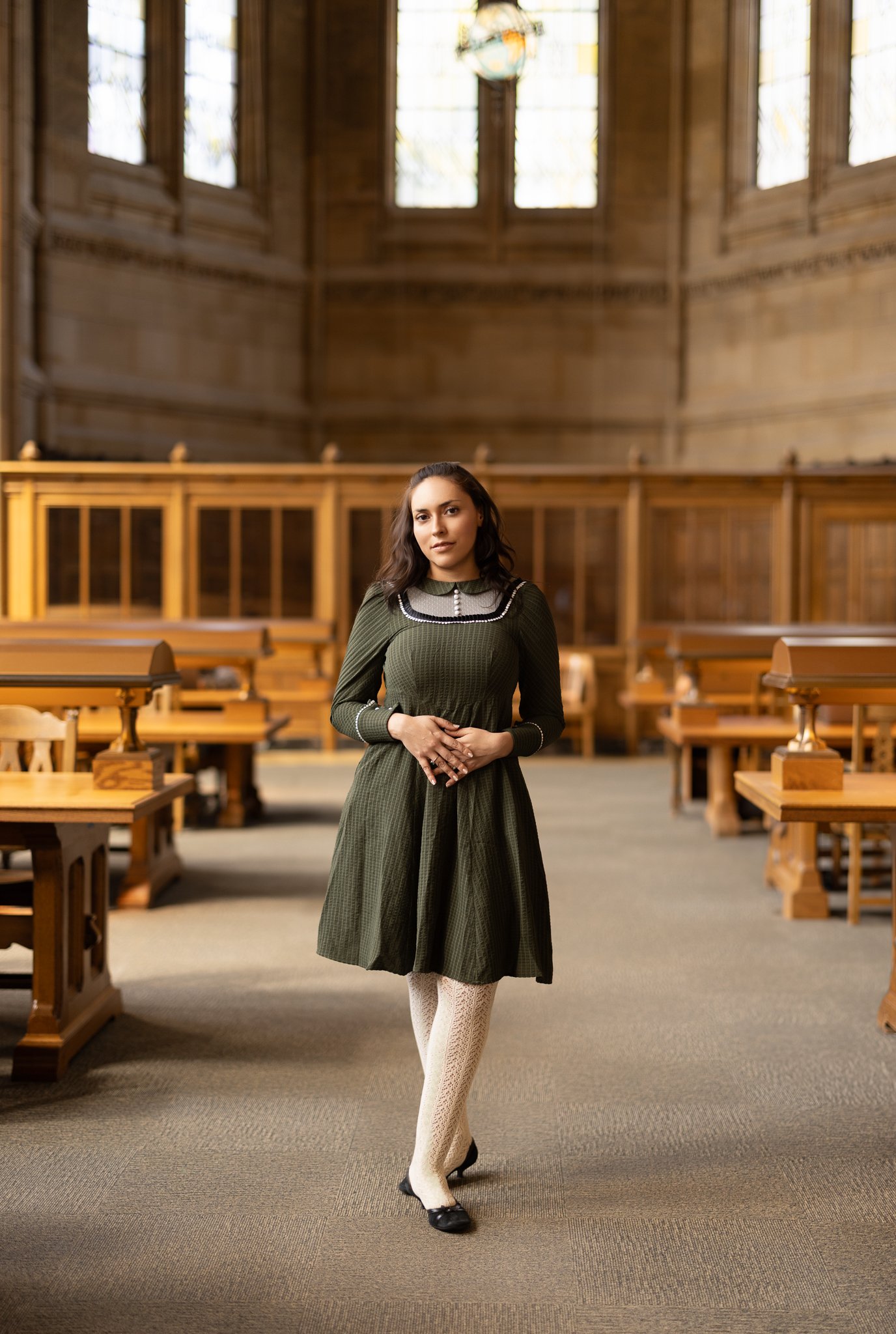 A woman standing inside a wooden courtroom or council chamber with high windows and wooden benches.
