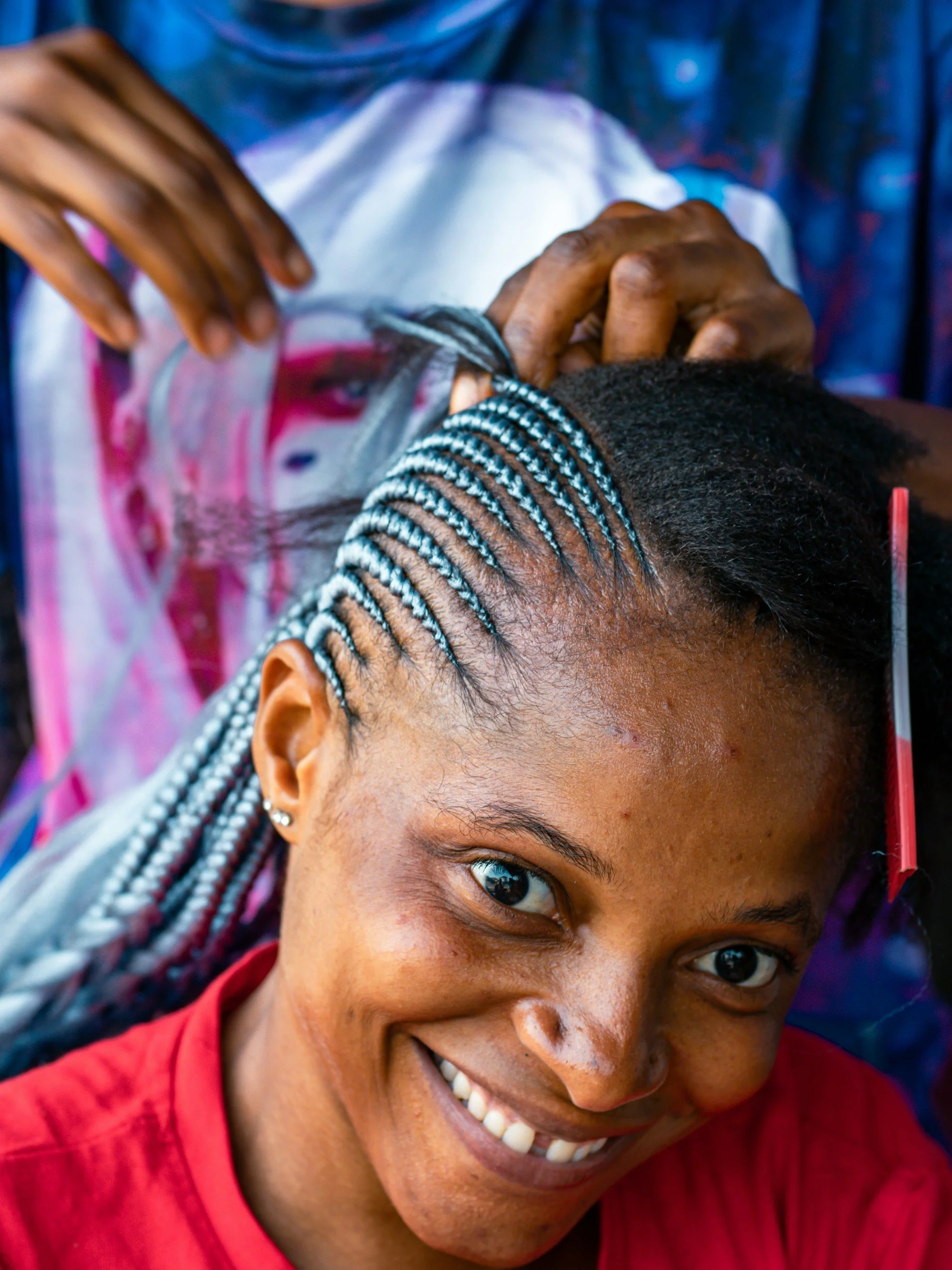 Young woman smiling while getting her hair styled with braids at a salon.
