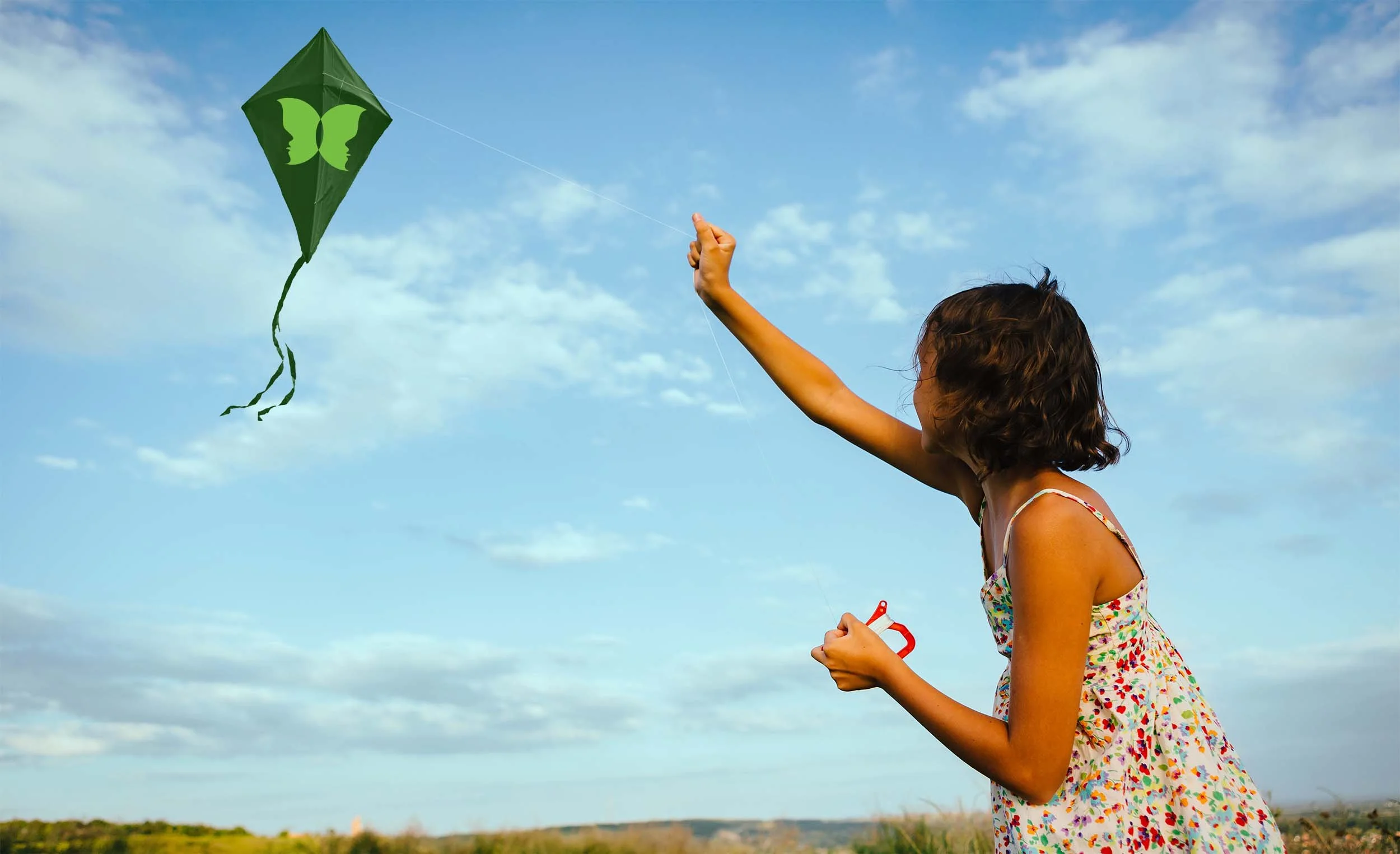 A young girl in a colorful dress flying a green kite with butterfly faces on it in an open field on a partly cloudy day.