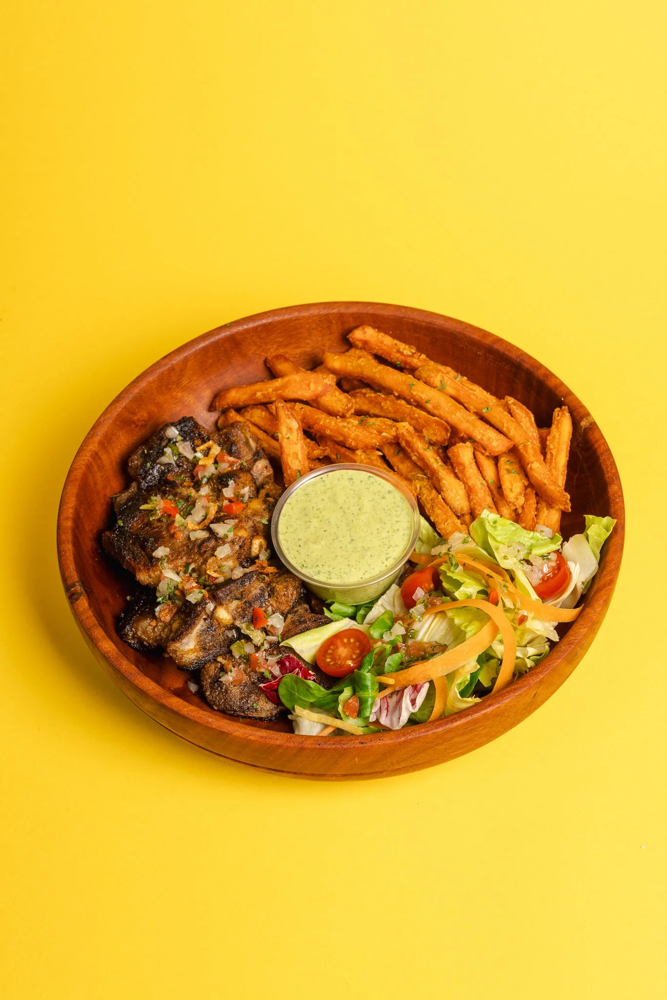 Bol de salade, frites, ailes de poulet avec sauce verte, et légumes, sur fond jaune